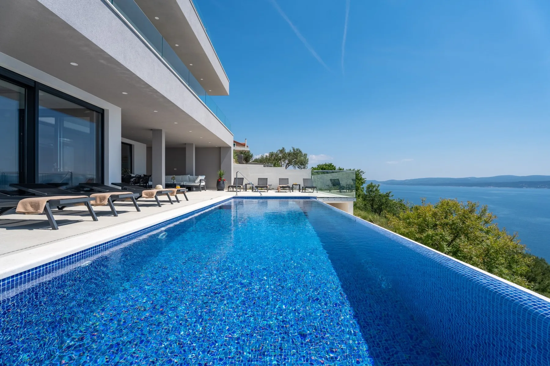 A swimming pool beside a modern building overlooks the sea.