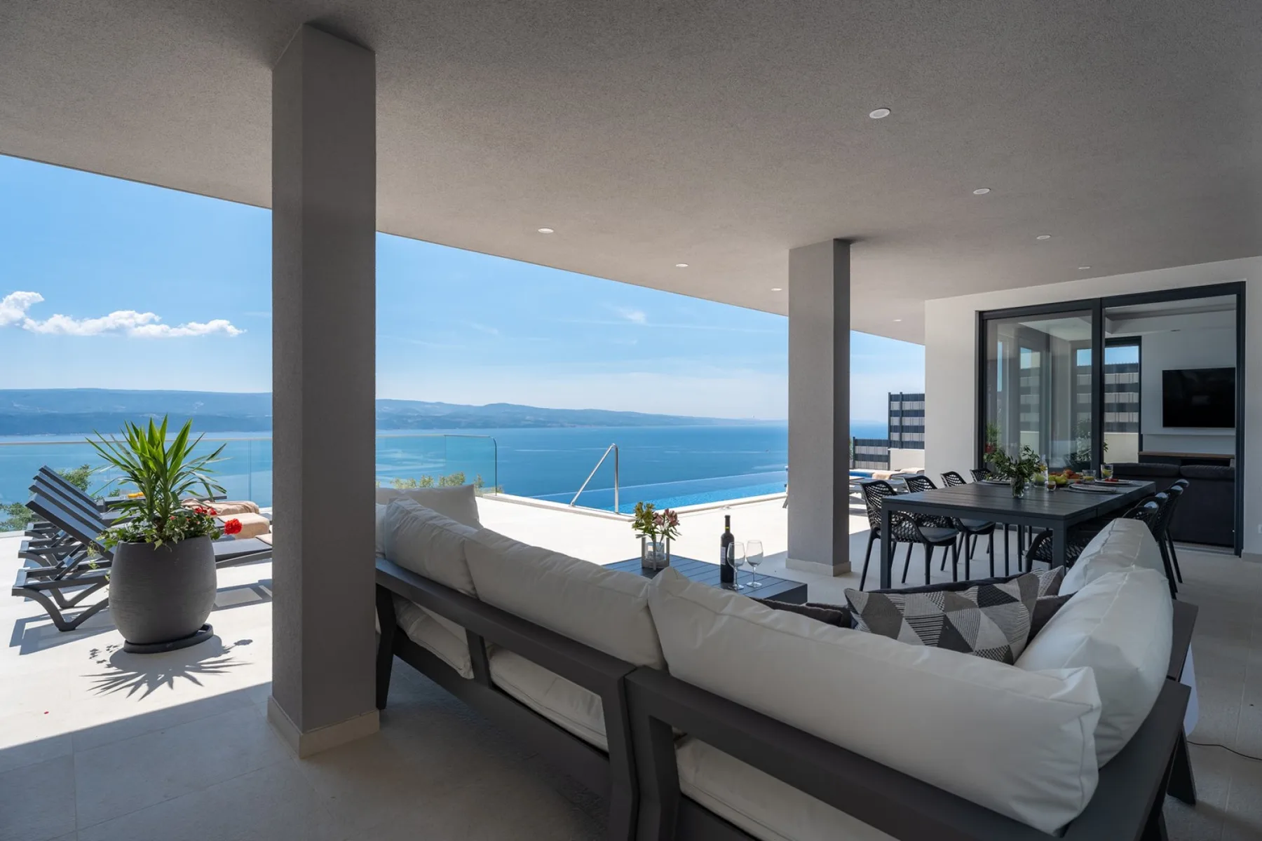 A covered terrace has lounge seating and a dining area overlooking the sea.