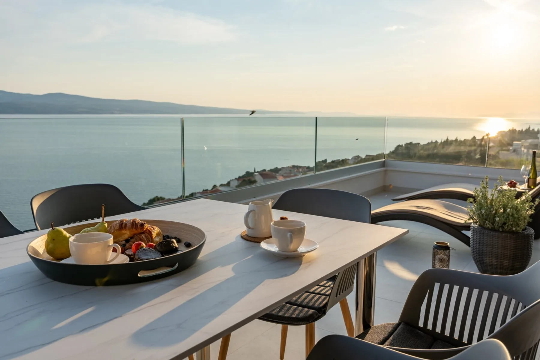 A seaside terrace dining area overlooks calm water in the warm evening light.