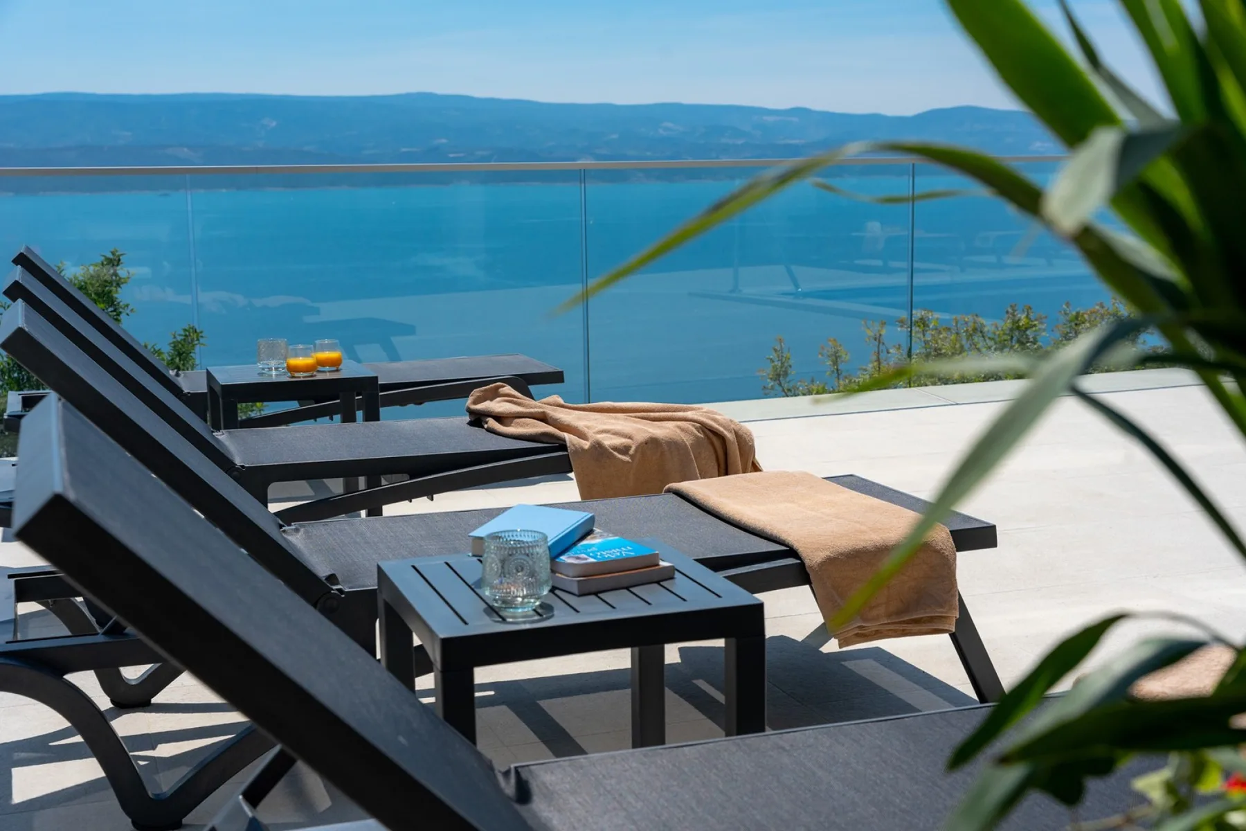 A sunny outdoor terrace with lounge seating overlooks a blue lake.