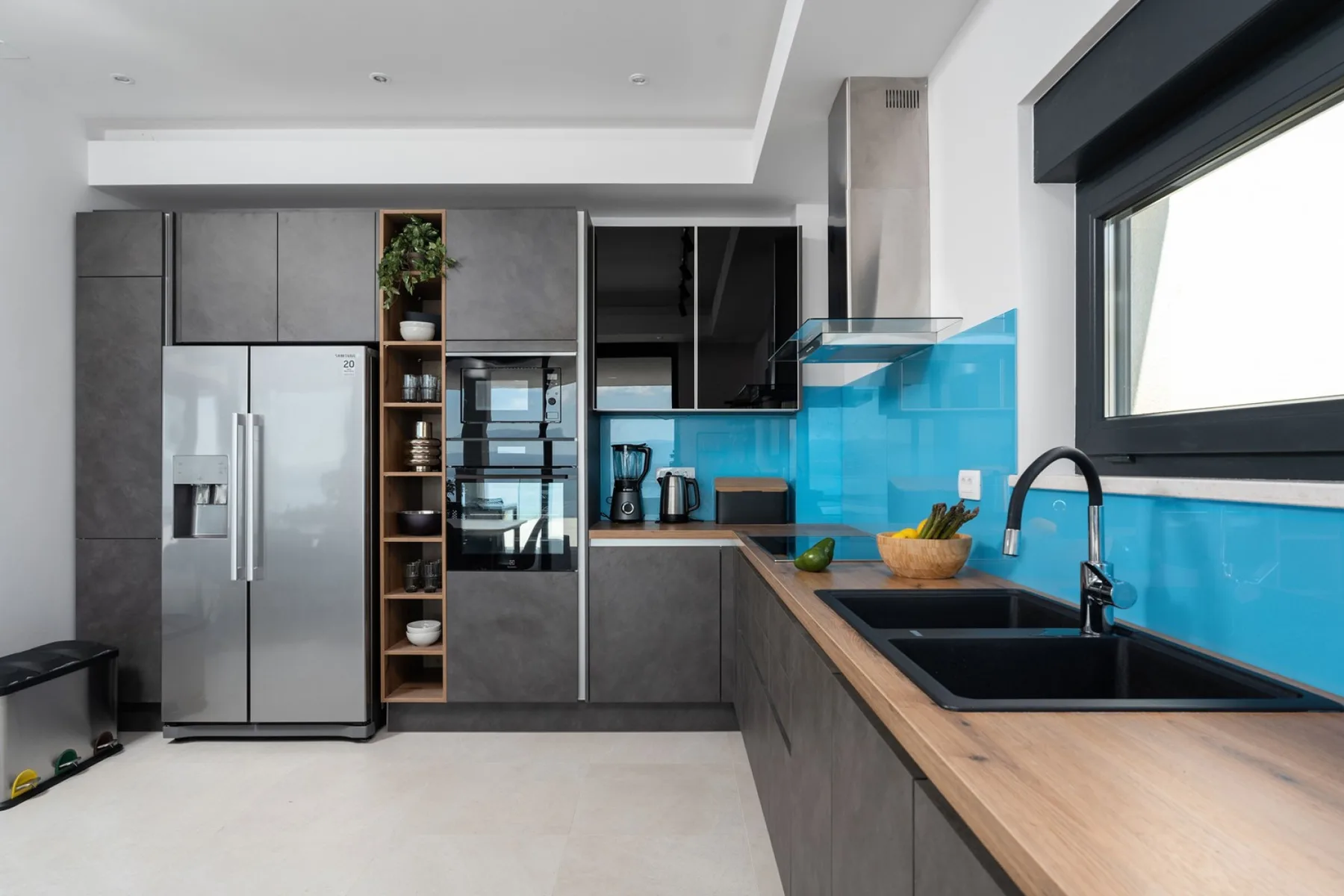 A modern kitchen with dark cabinets, stainless steel appliances, and a bright blue backsplash.