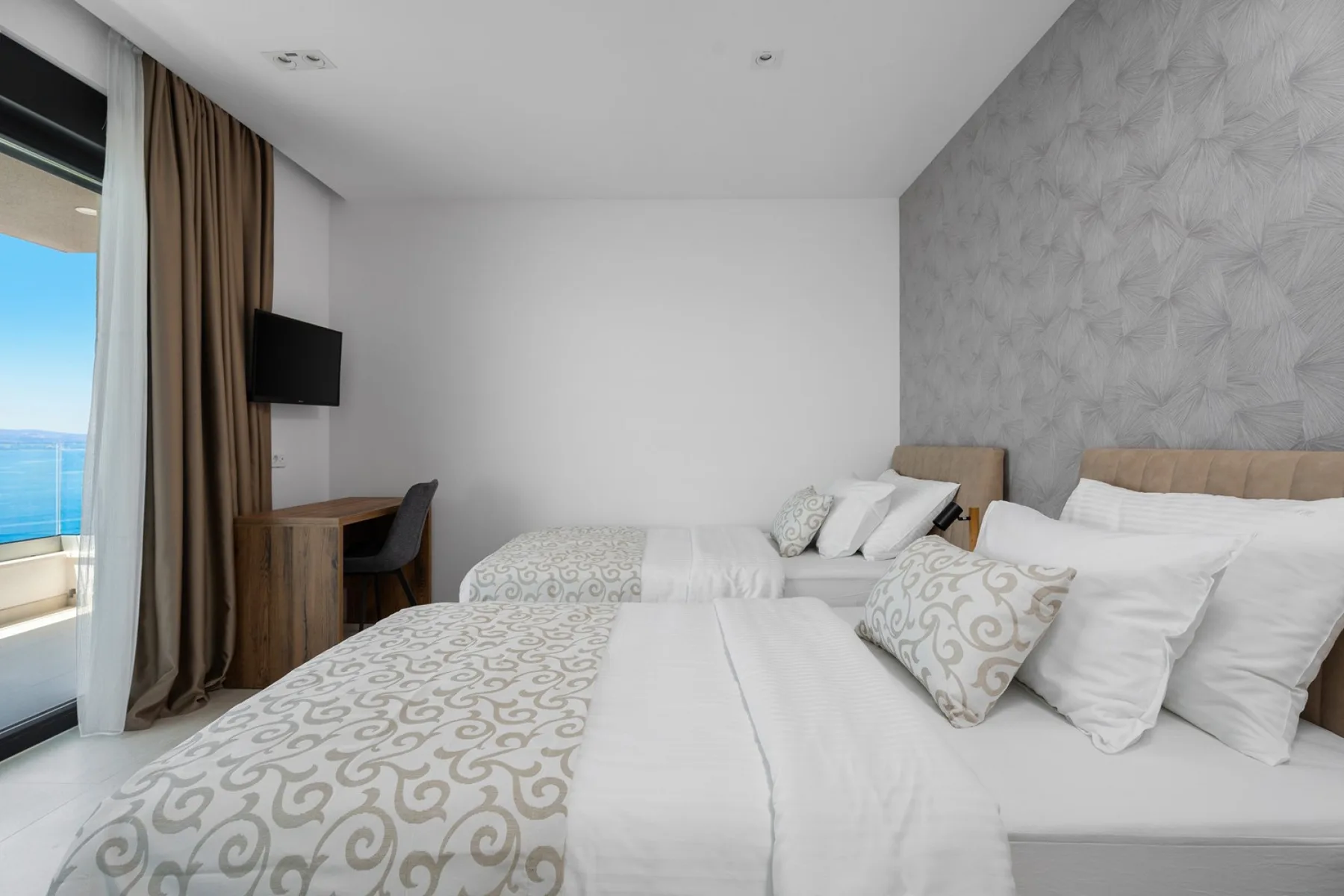 A bright bedroom with two beds and a sliding glass door opening onto a balcony.
