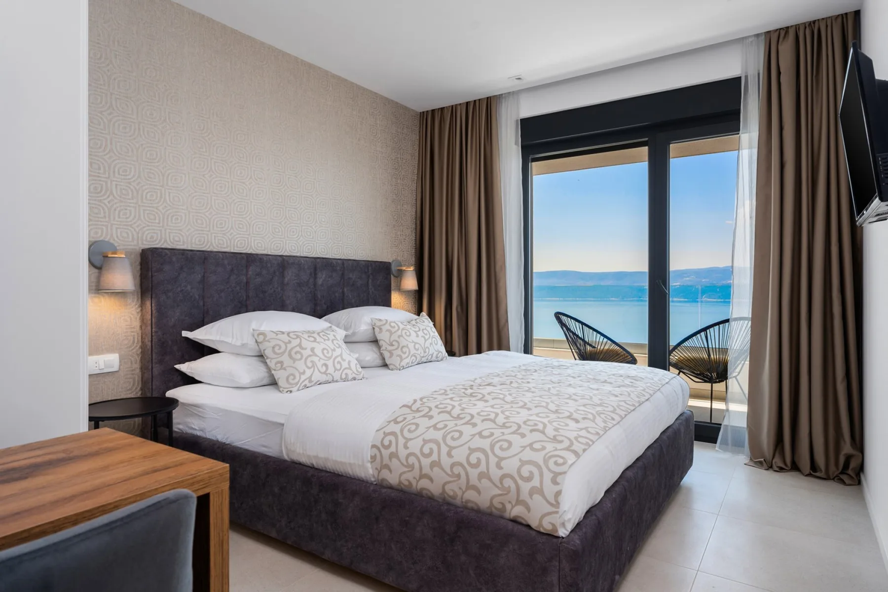 A bedroom with a large bed beside glass doors overlooking the sea.