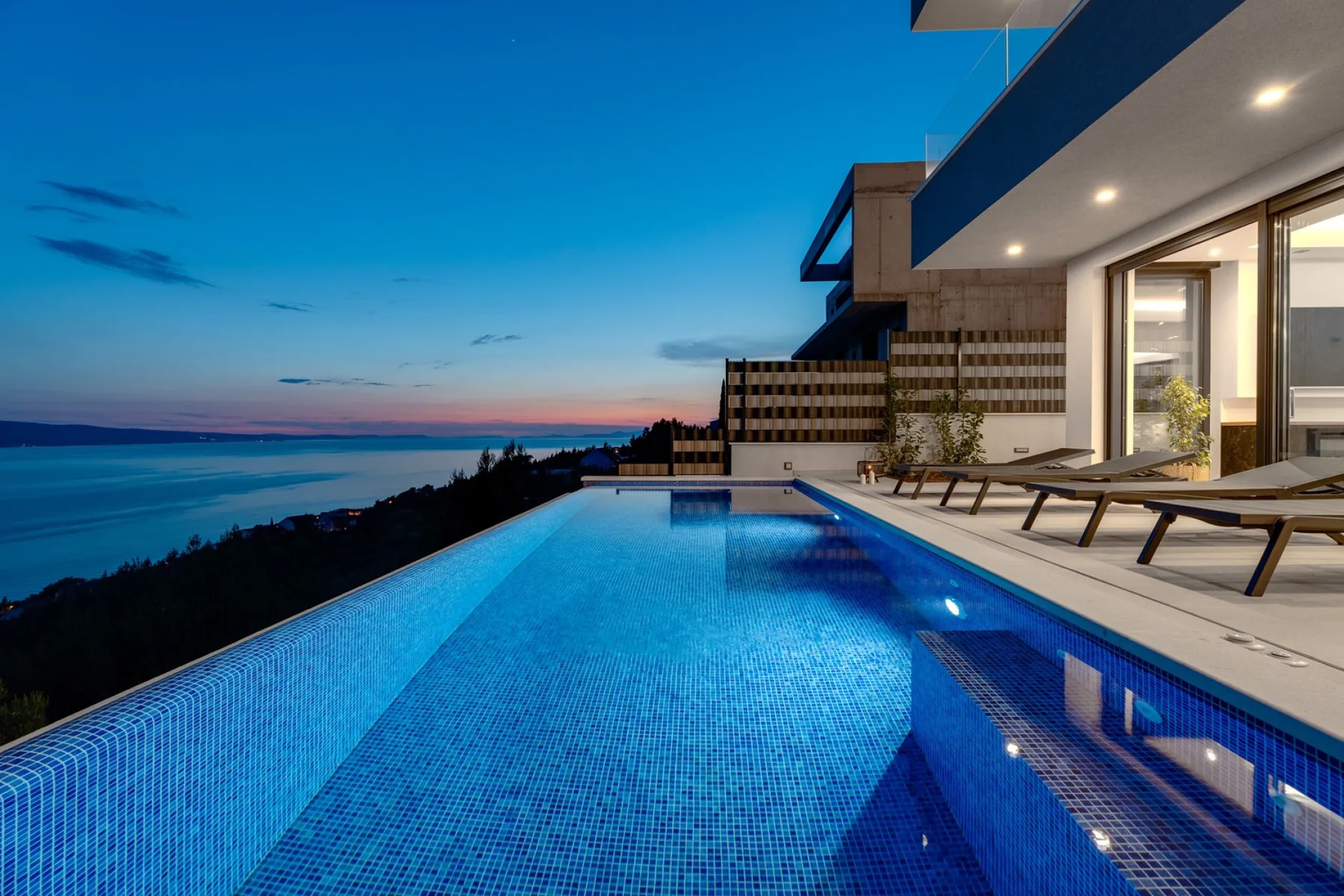 A swimming pool beside a modern terrace overlooks the water at dusk.