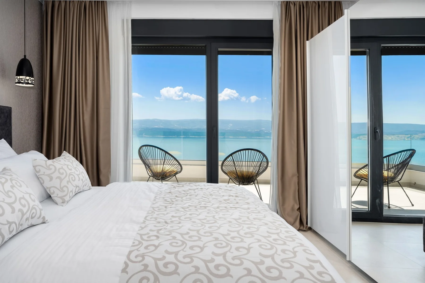 A bedroom with a bed facing large windows overlooking the sea.