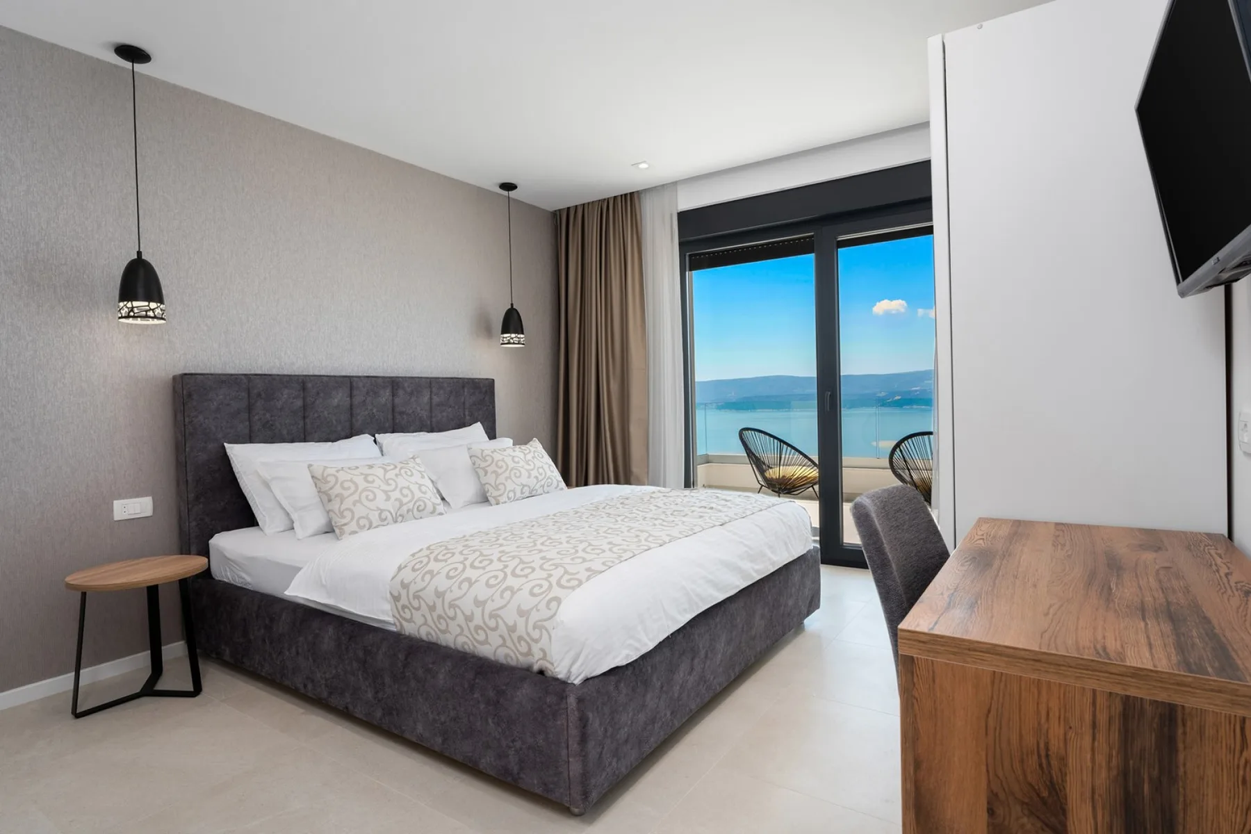 A bedroom with a large bed beside sliding glass doors overlooking the sea.