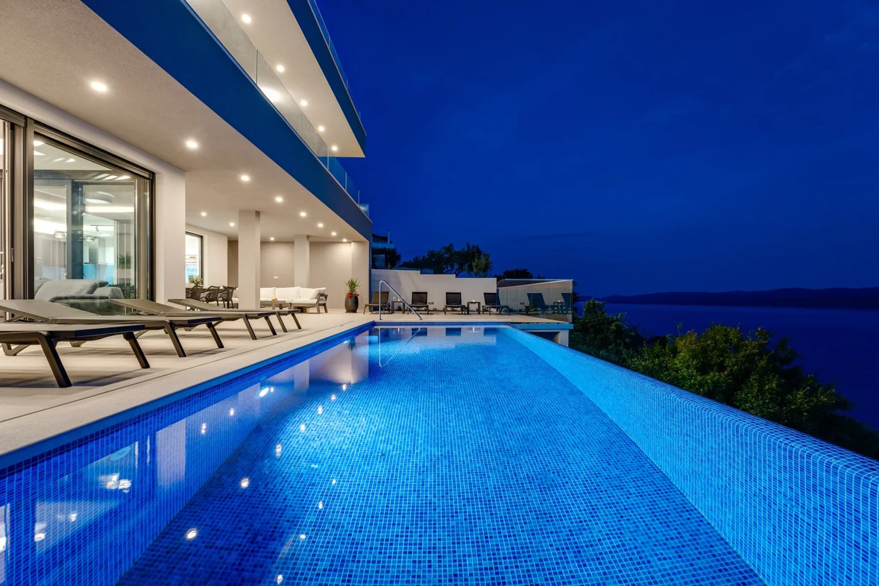 An illuminated outdoor swimming pool beside a modern building at dusk.