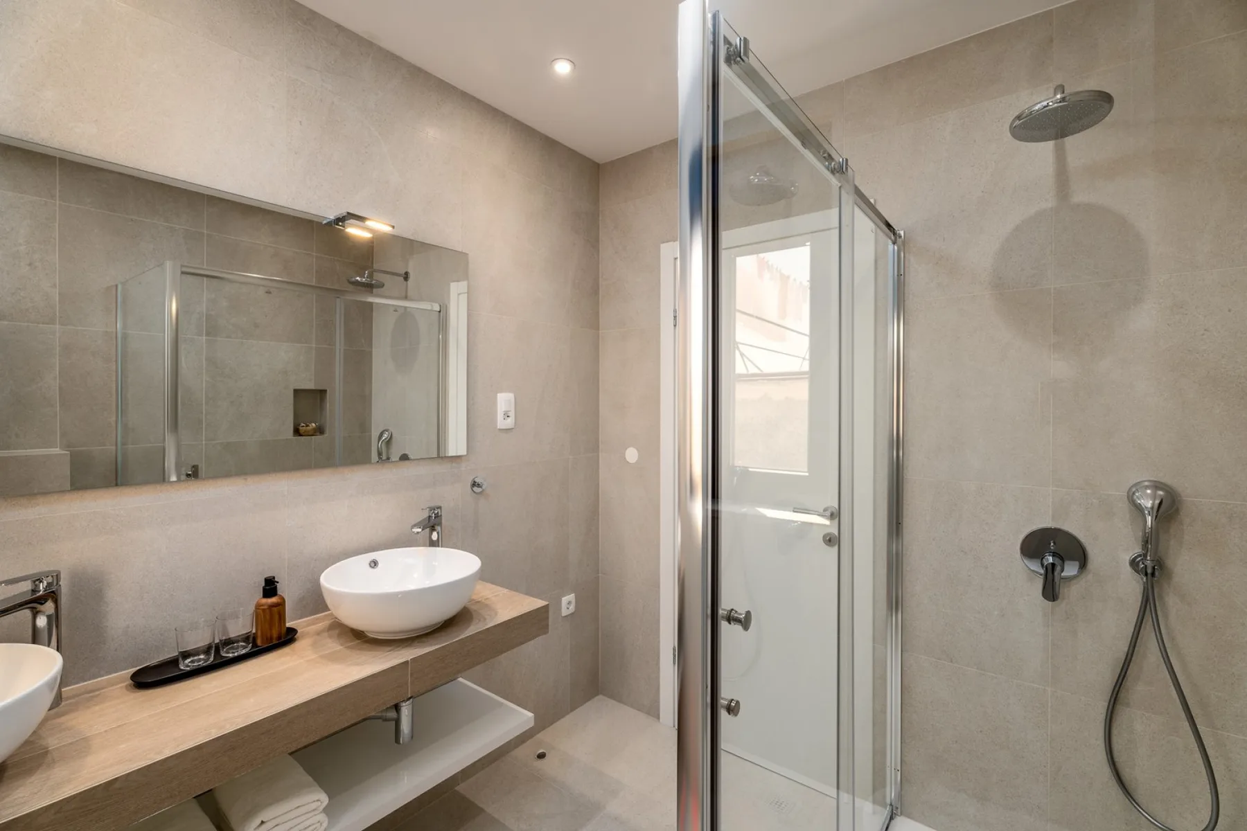 A tiled bathroom with a glass shower and a long vanity.