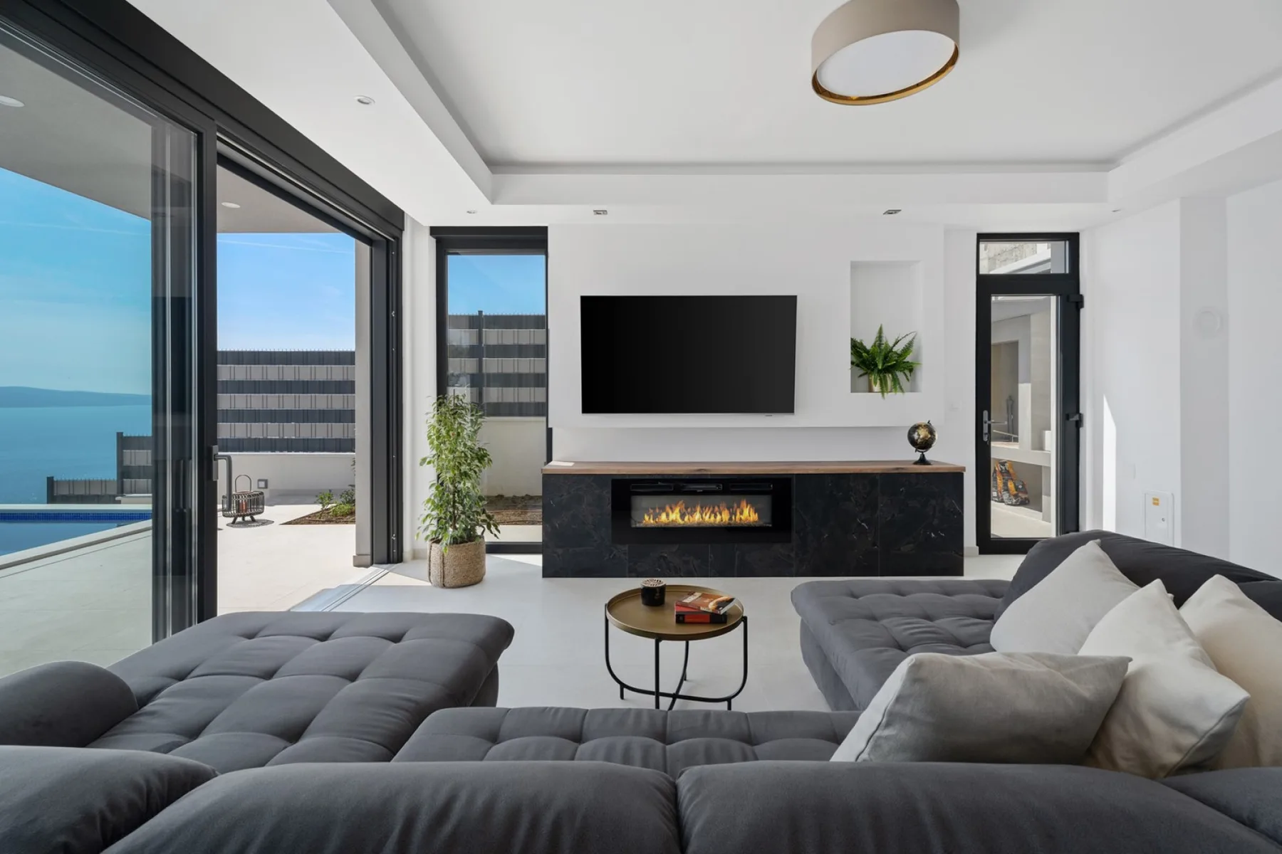 A modern living room with gray seating, a television, and large glass doors.