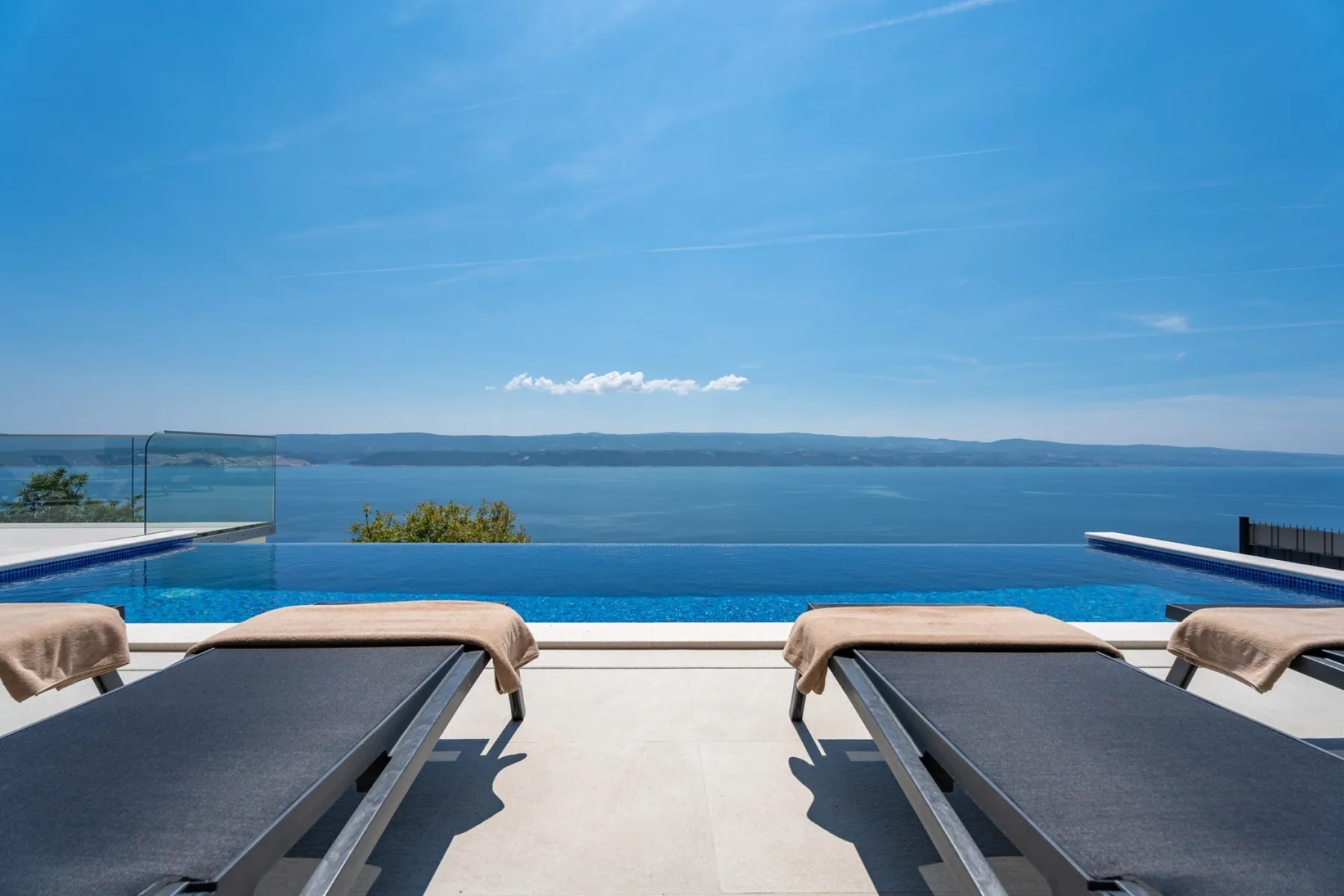A poolside terrace overlooks the water, with sun loungers arranged beside the pool.