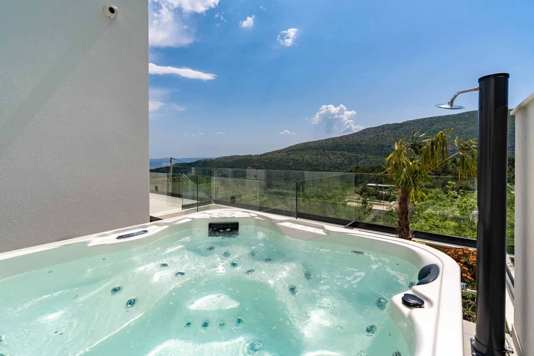 An outdoor hot tub overlooks a green hillside beneath a clear blue sky.