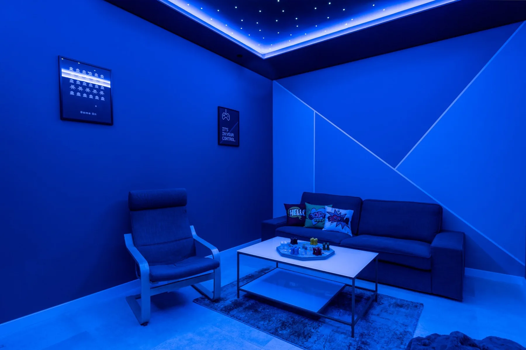 A blue-lit lounge has a sofa, an armchair, and a low table.
