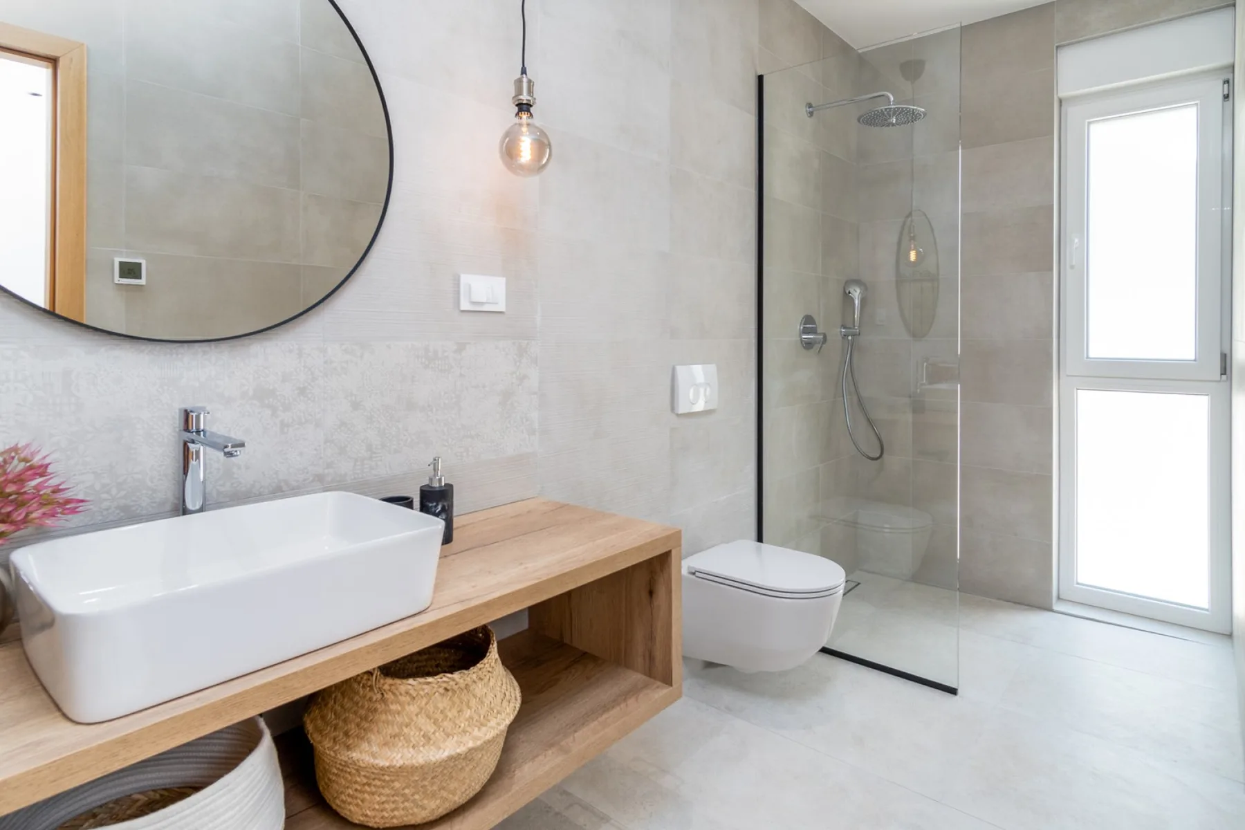 A modern bathroom with a sink, wall-mounted toilet, and glass shower.