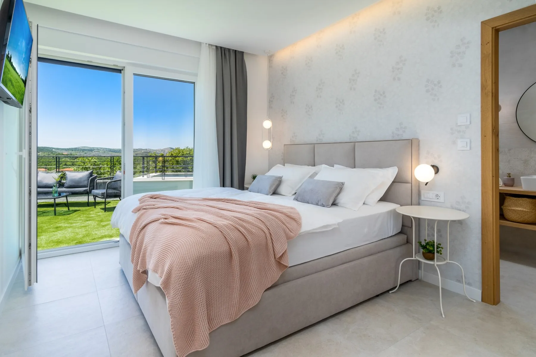 A bright bedroom with a large bed and sliding glass doors opening onto a terrace.