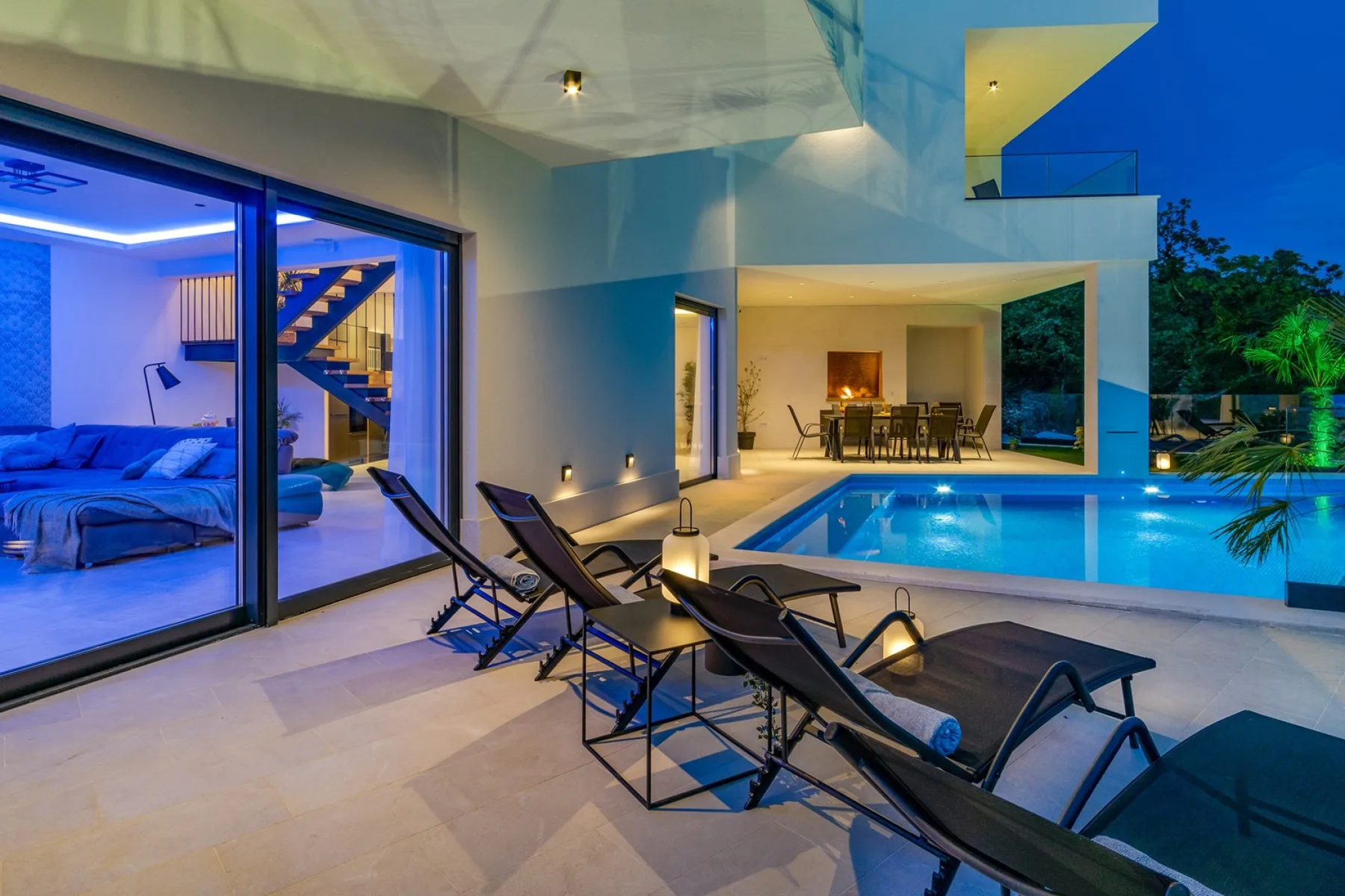 A modern poolside patio with lounge seating beside a glass-walled living area.