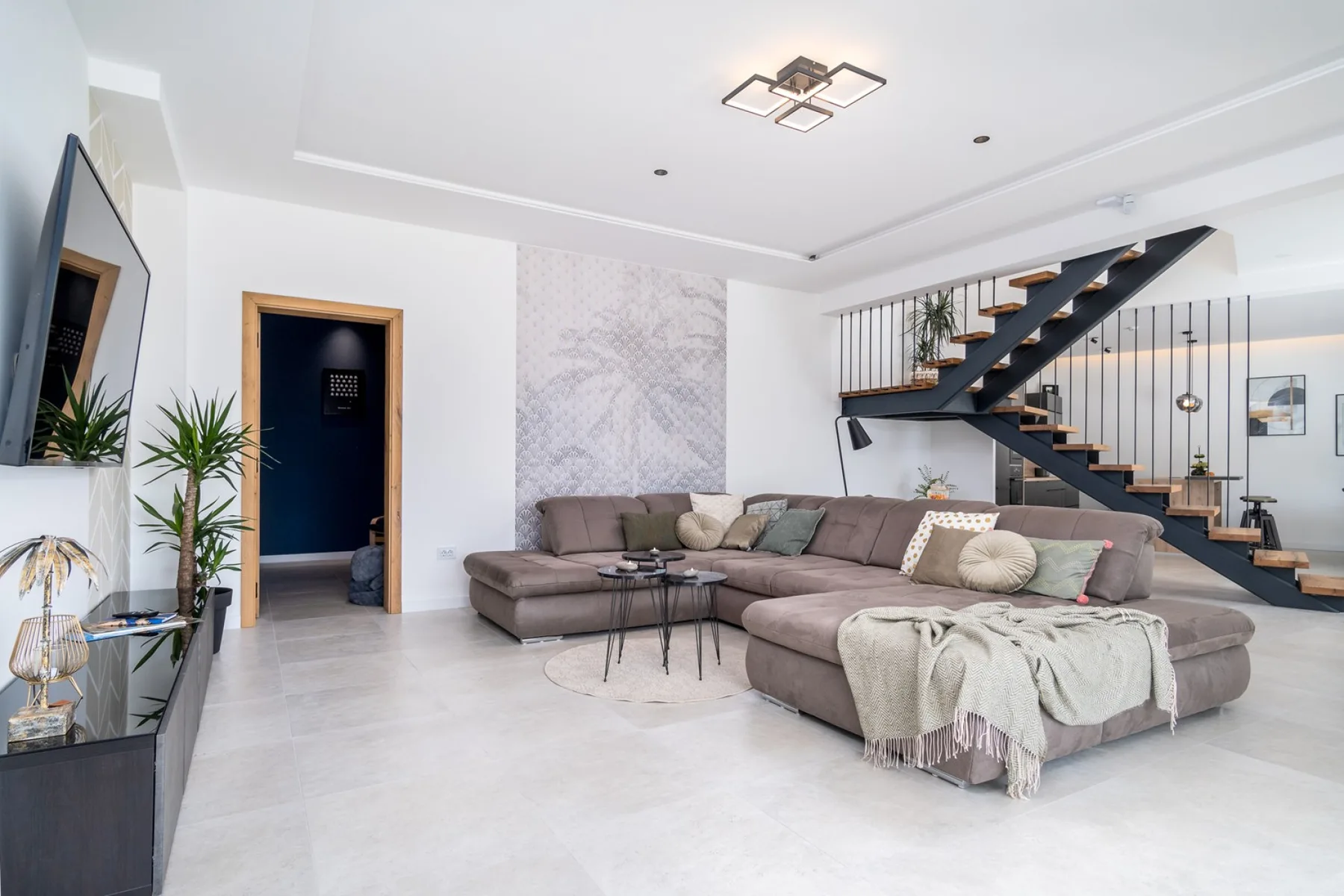 A bright living room features a large sectional seating area and an open staircase.