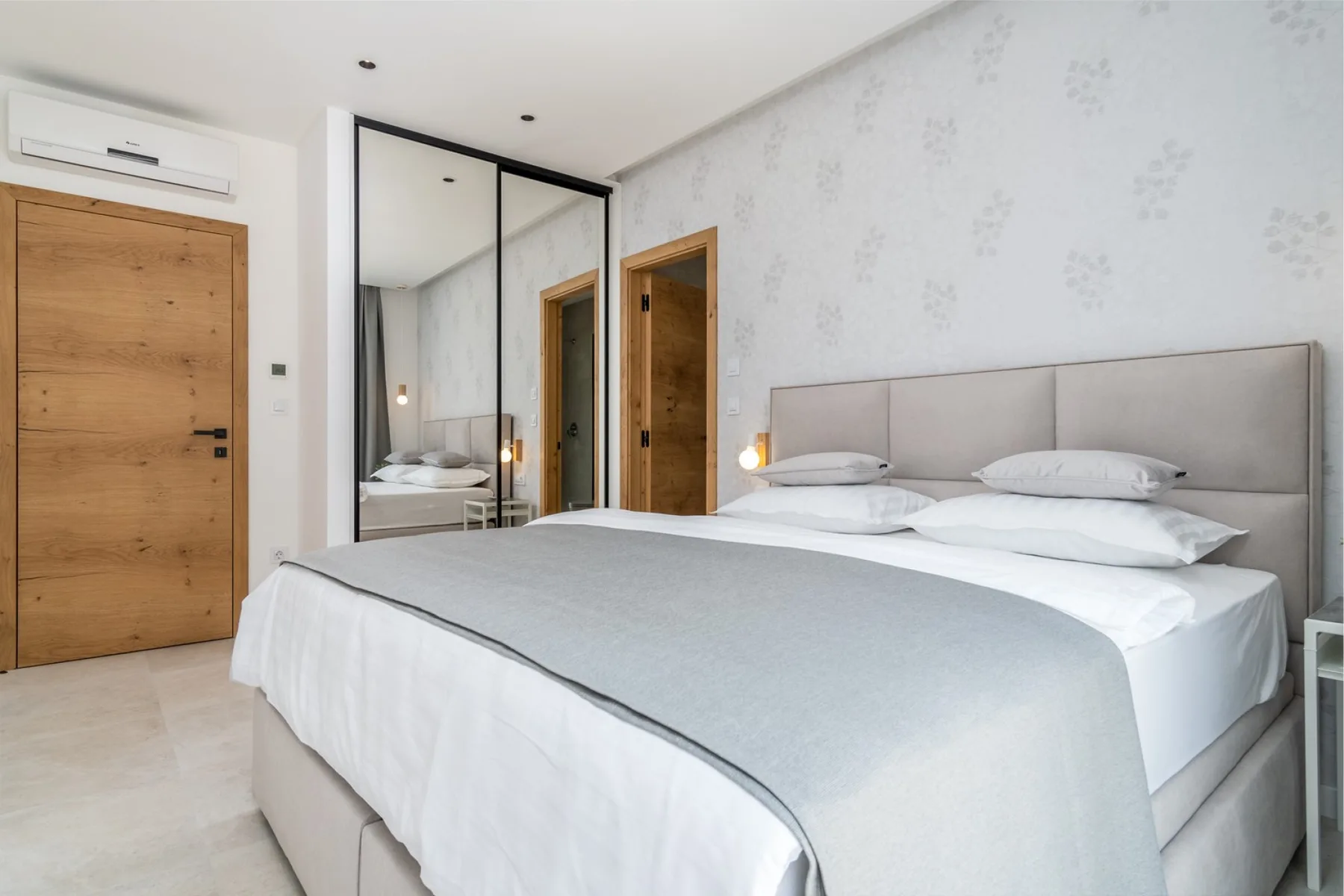 A bedroom with a neatly made bed and mirrored wardrobe.