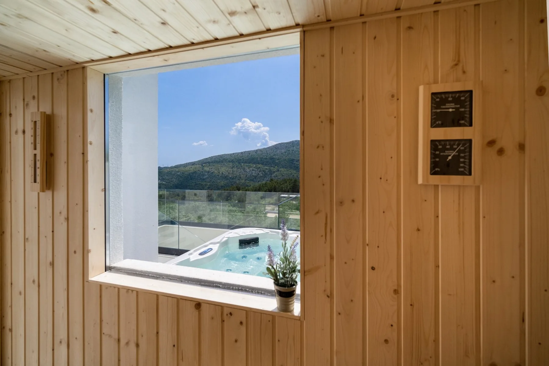 A wood-paneled sauna interior with a window overlooking hills and an outdoor pool.