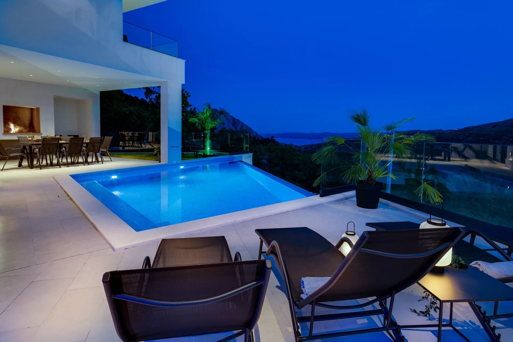 An outdoor swimming pool beside a terrace with lounge seating at dusk.