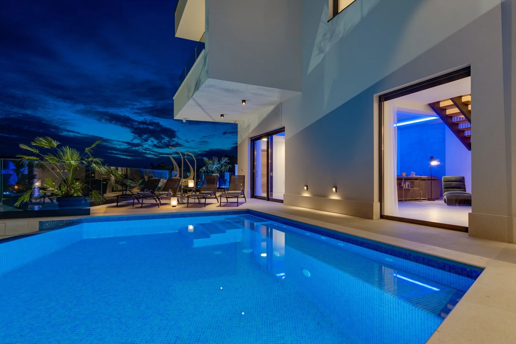 A swimming pool beside a modern building, with outdoor seating visible at dusk.