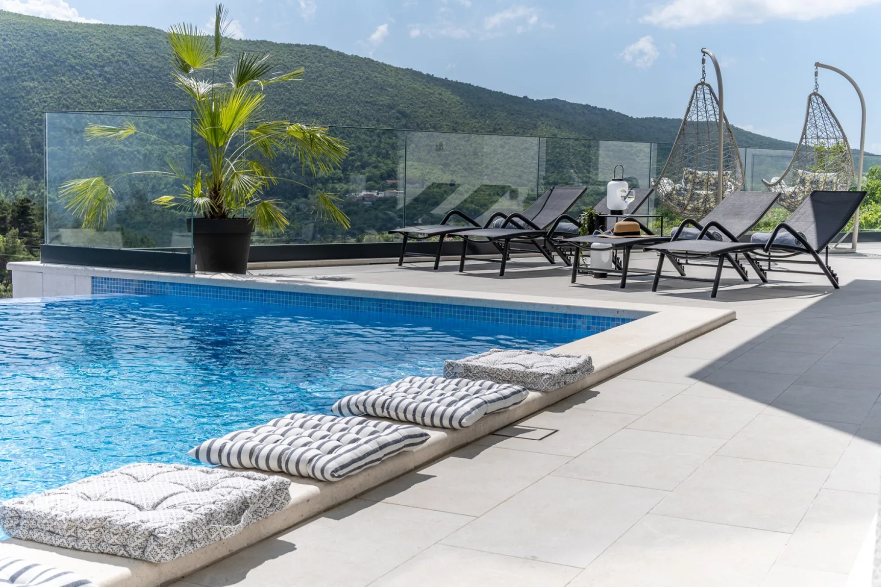 An outdoor swimming pool is bordered by lounge seating and overlooks green hills.