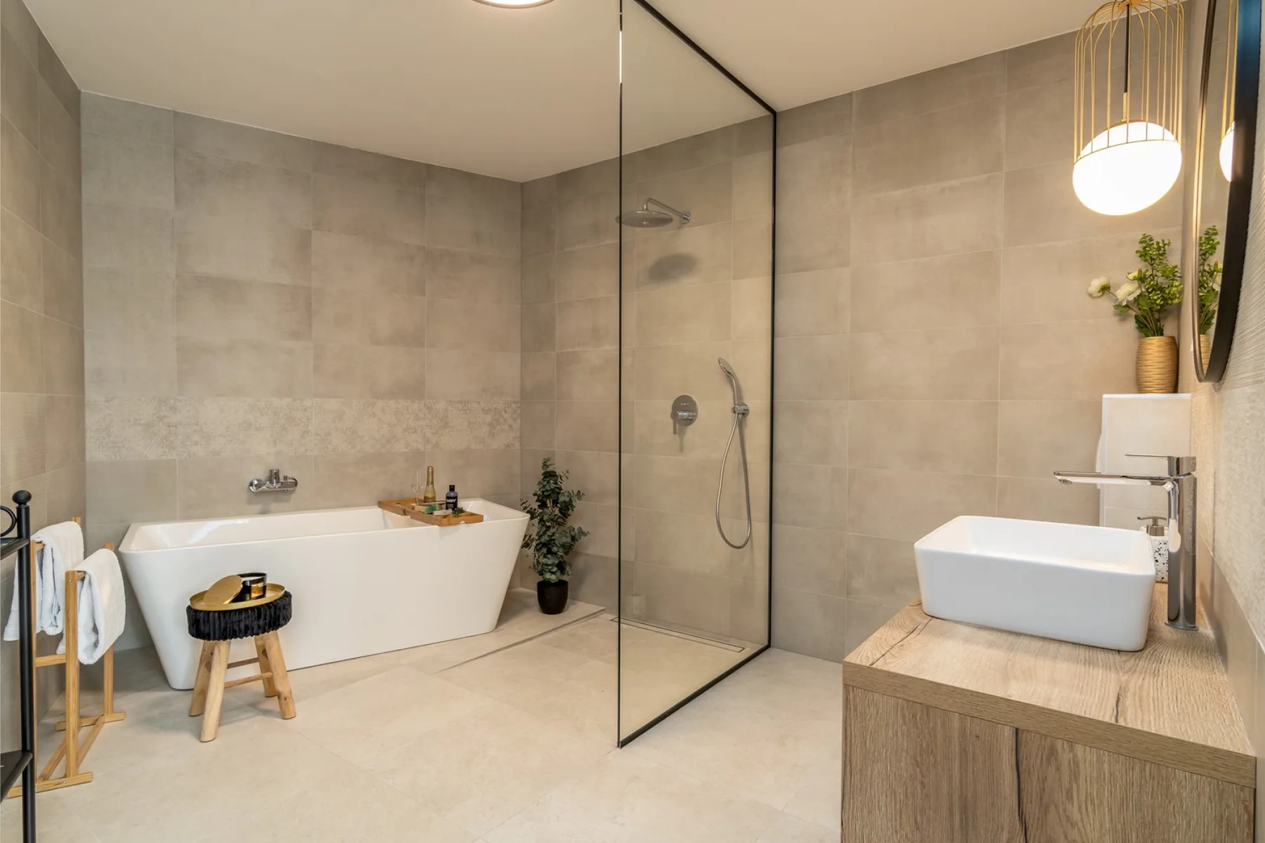 A tiled bathroom features a freestanding bathtub, glass shower screen, and vanity.