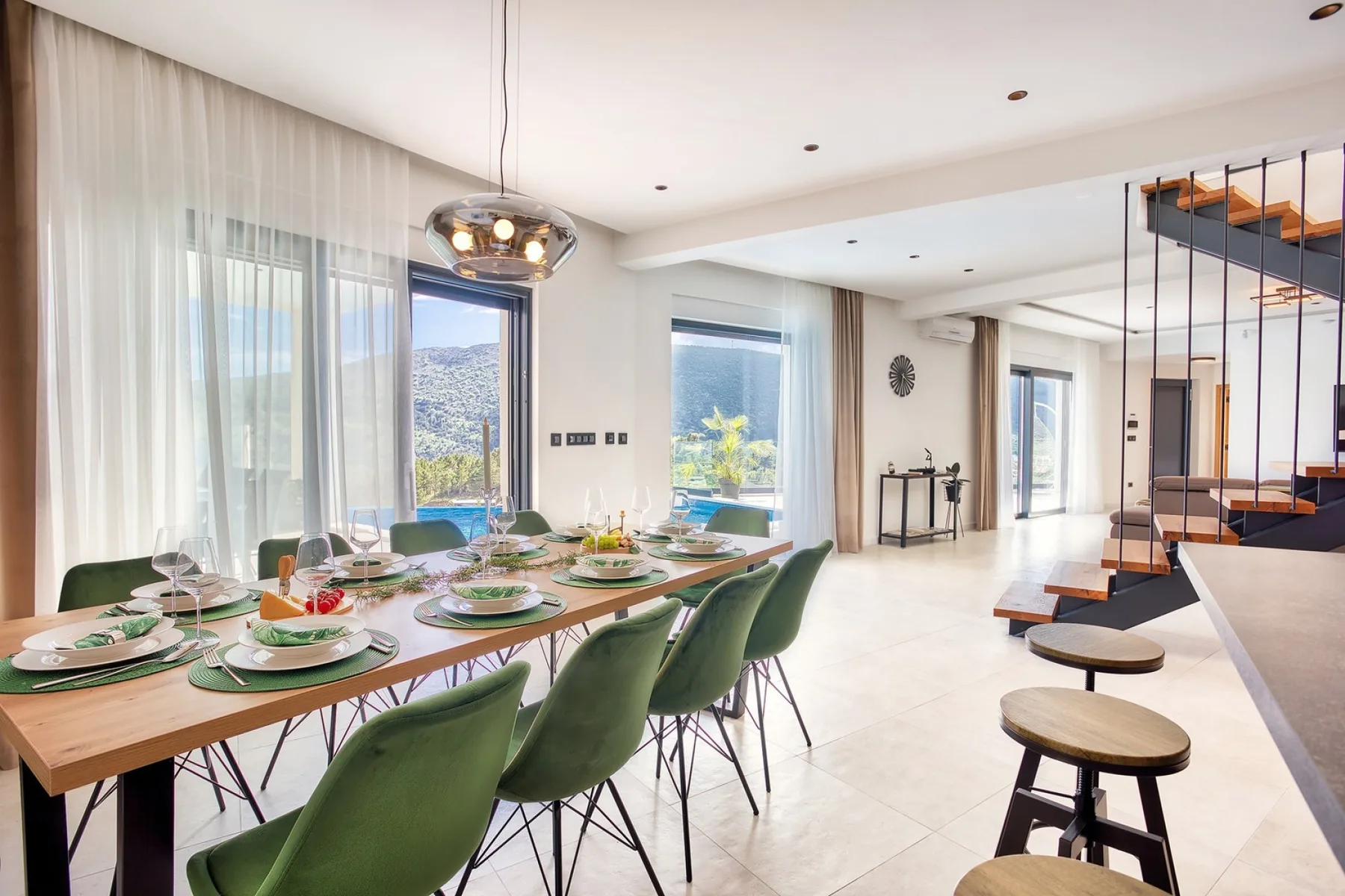 A bright dining area with a long table set beside large windows and a staircase.