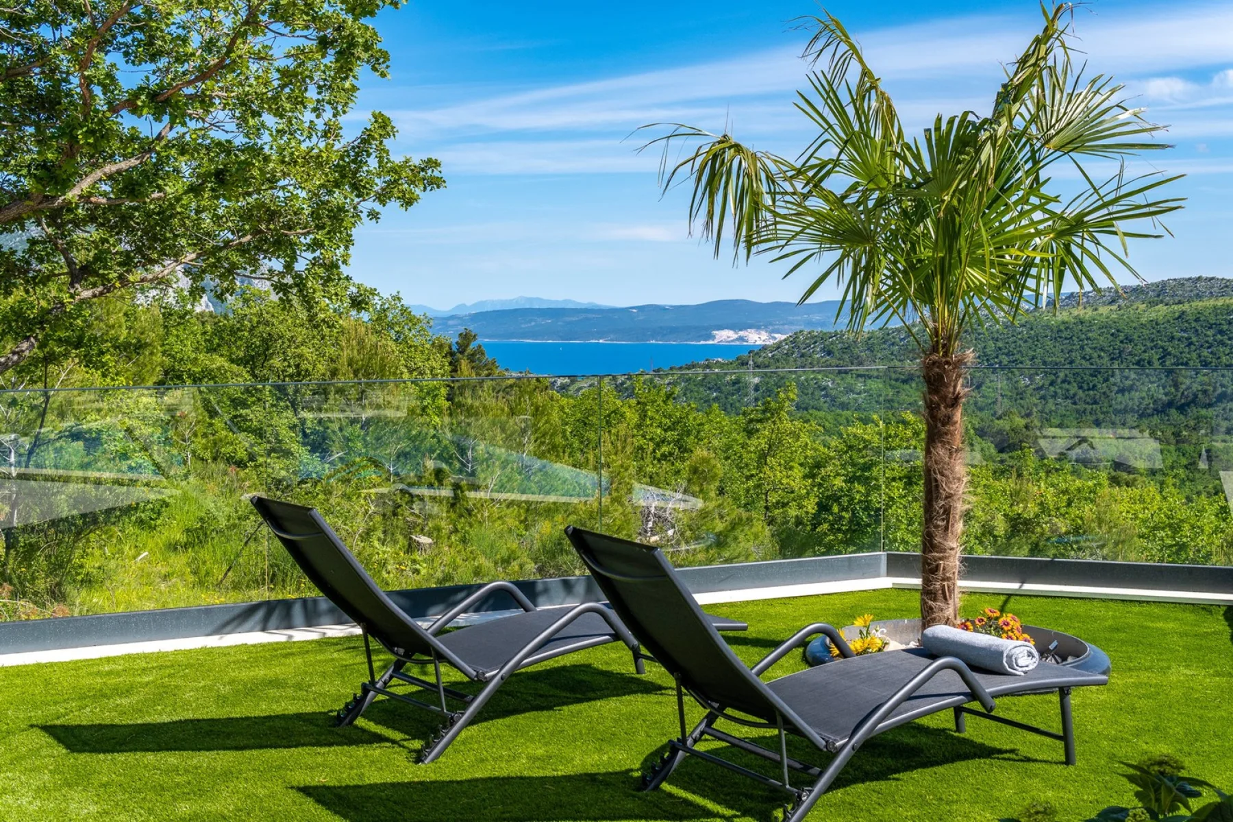 Outdoor seating overlooks a green hillside and the sea.