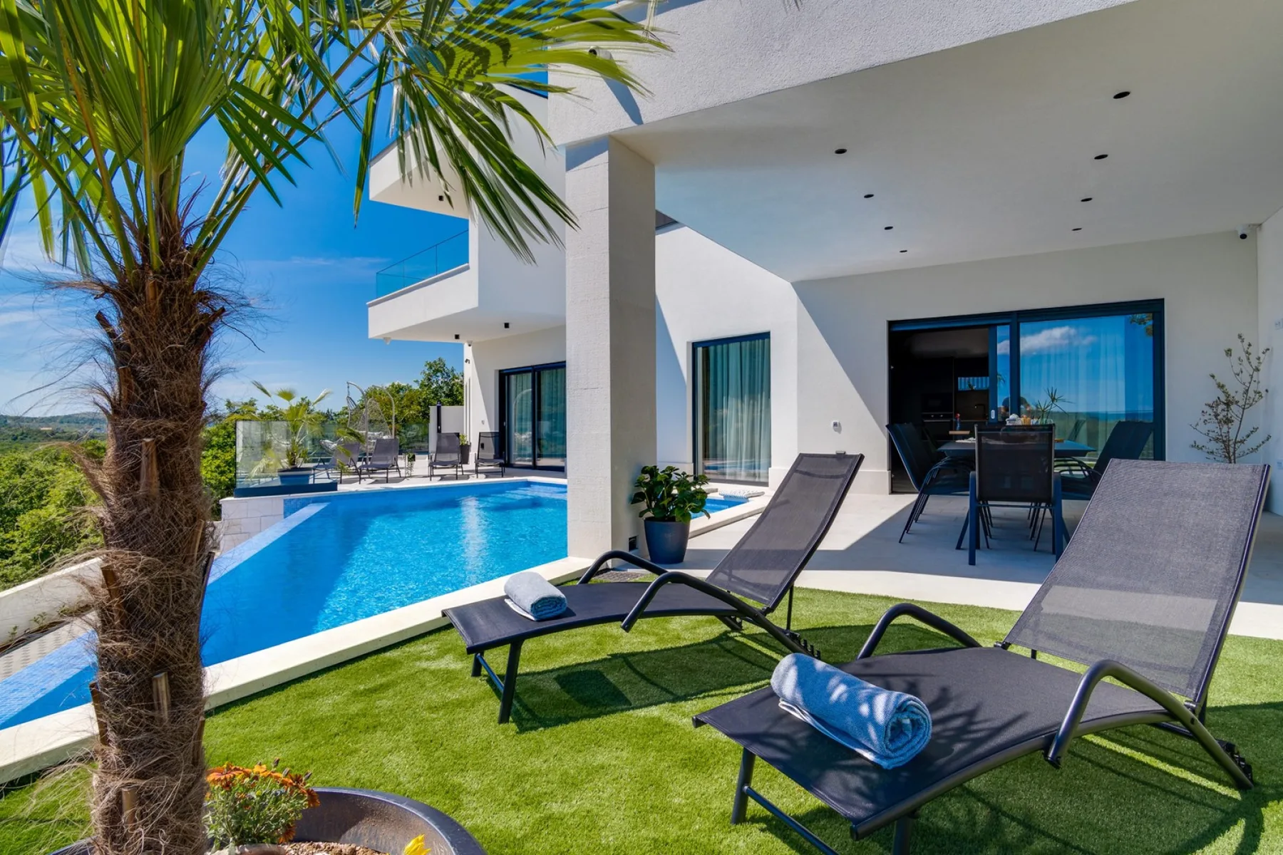 A modern house opens onto a poolside patio with lounge seating.