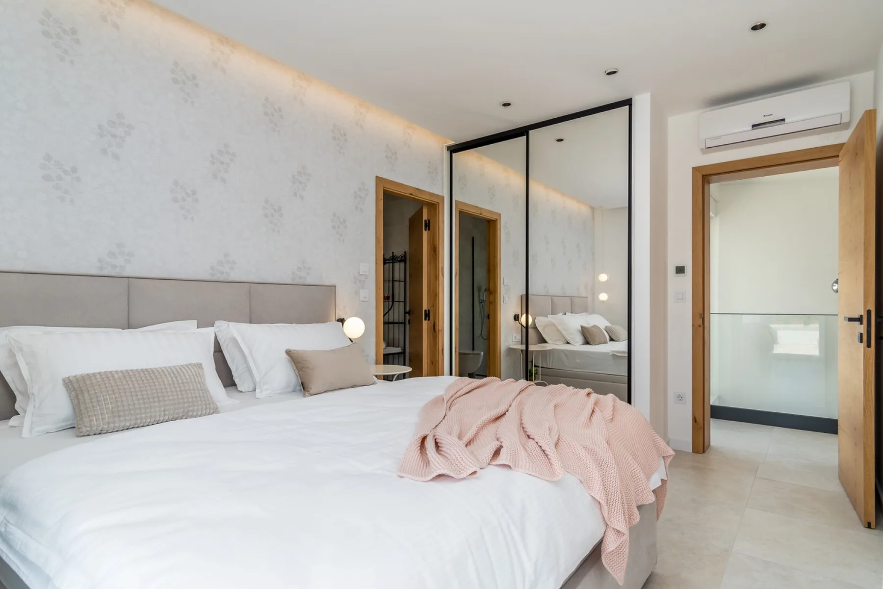 A bedroom with a large bed, mirrored wardrobe, and an open doorway.