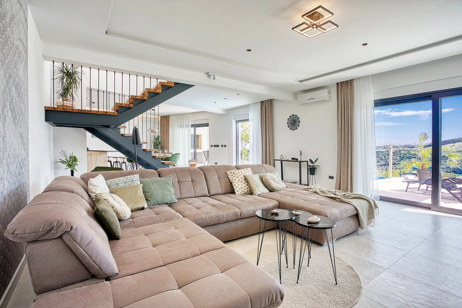A spacious living room with sectional seating, a staircase, and large glass doors.