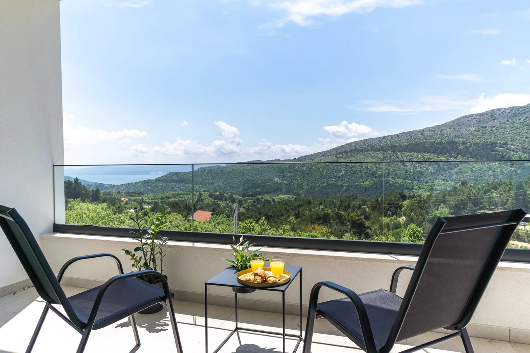 A balcony seating area overlooks green hills and a distant body of water.