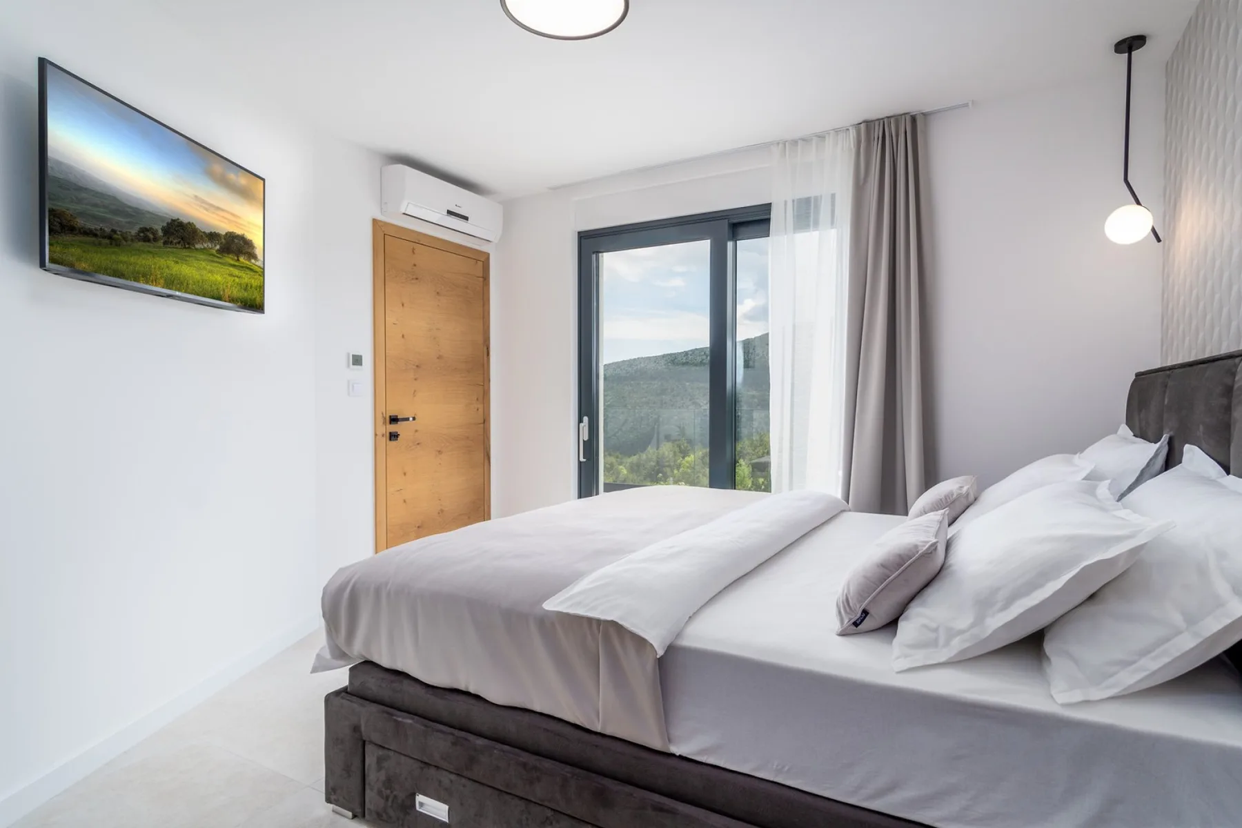 A bright bedroom with a large bed facing a window overlooking green hills.