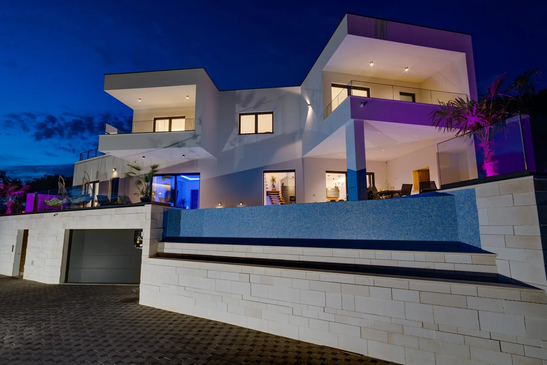 A modern house exterior at night, illuminated against a blue evening sky.