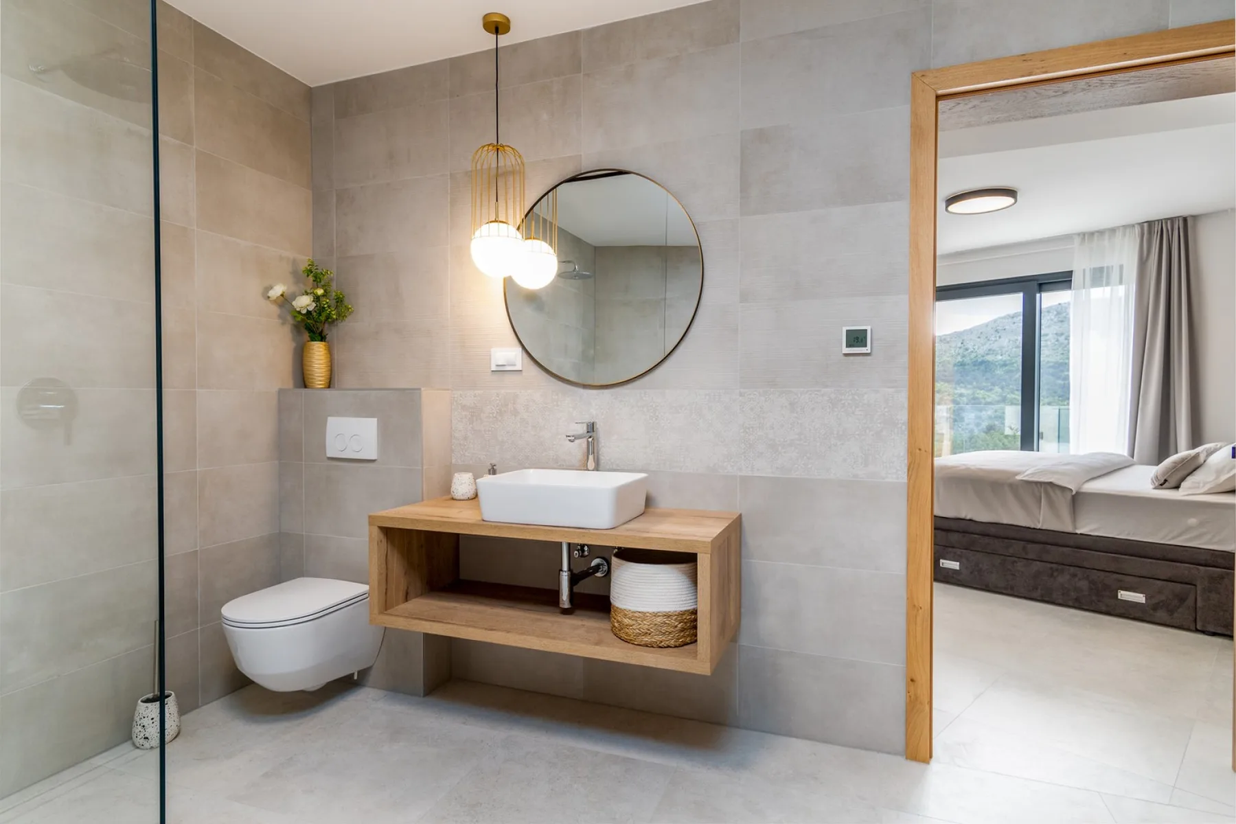 A tiled bathroom with a wooden vanity and a bedroom visible through the doorway.
