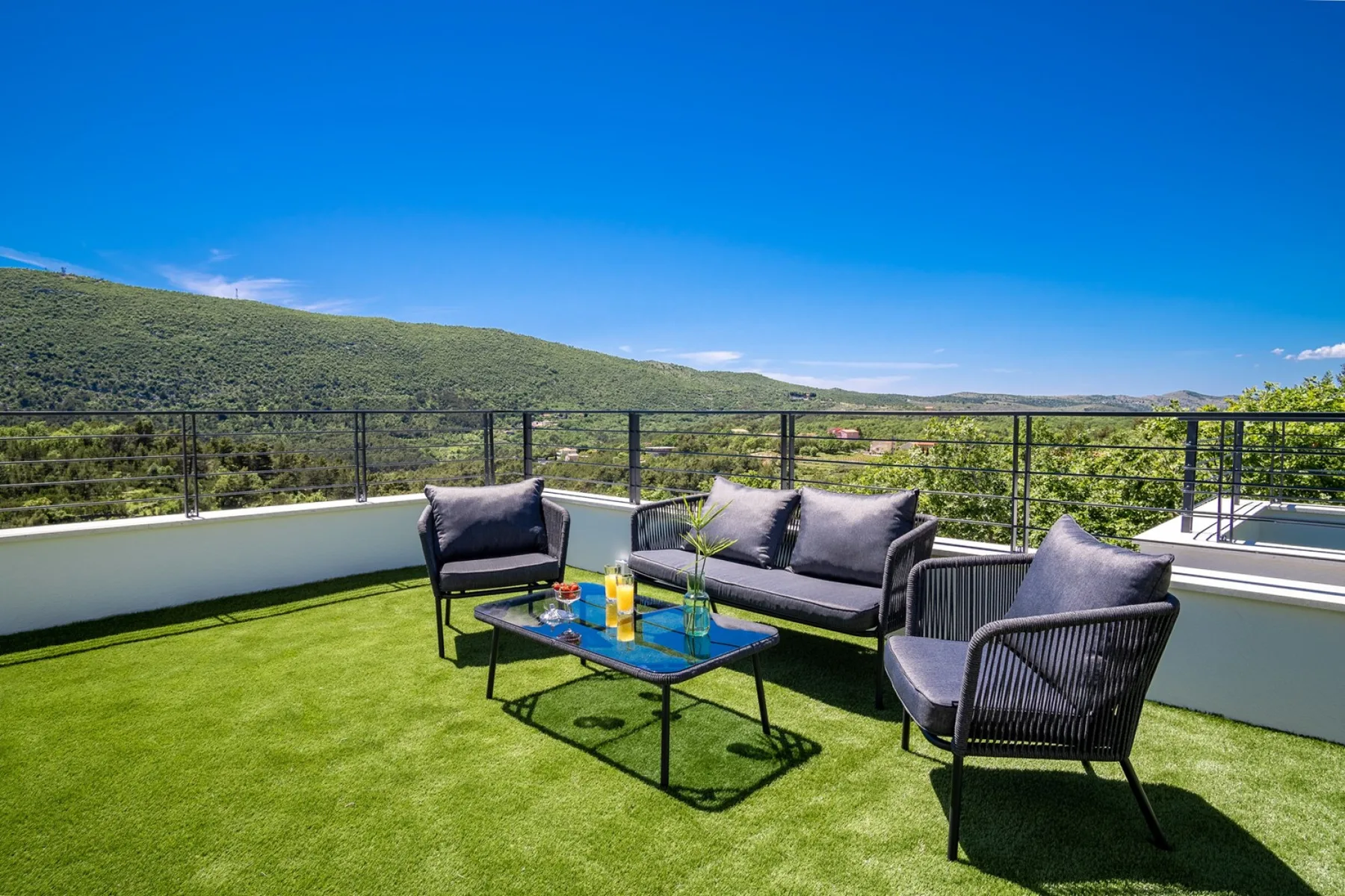 A rooftop terrace with outdoor seating and a table overlooks green hills.