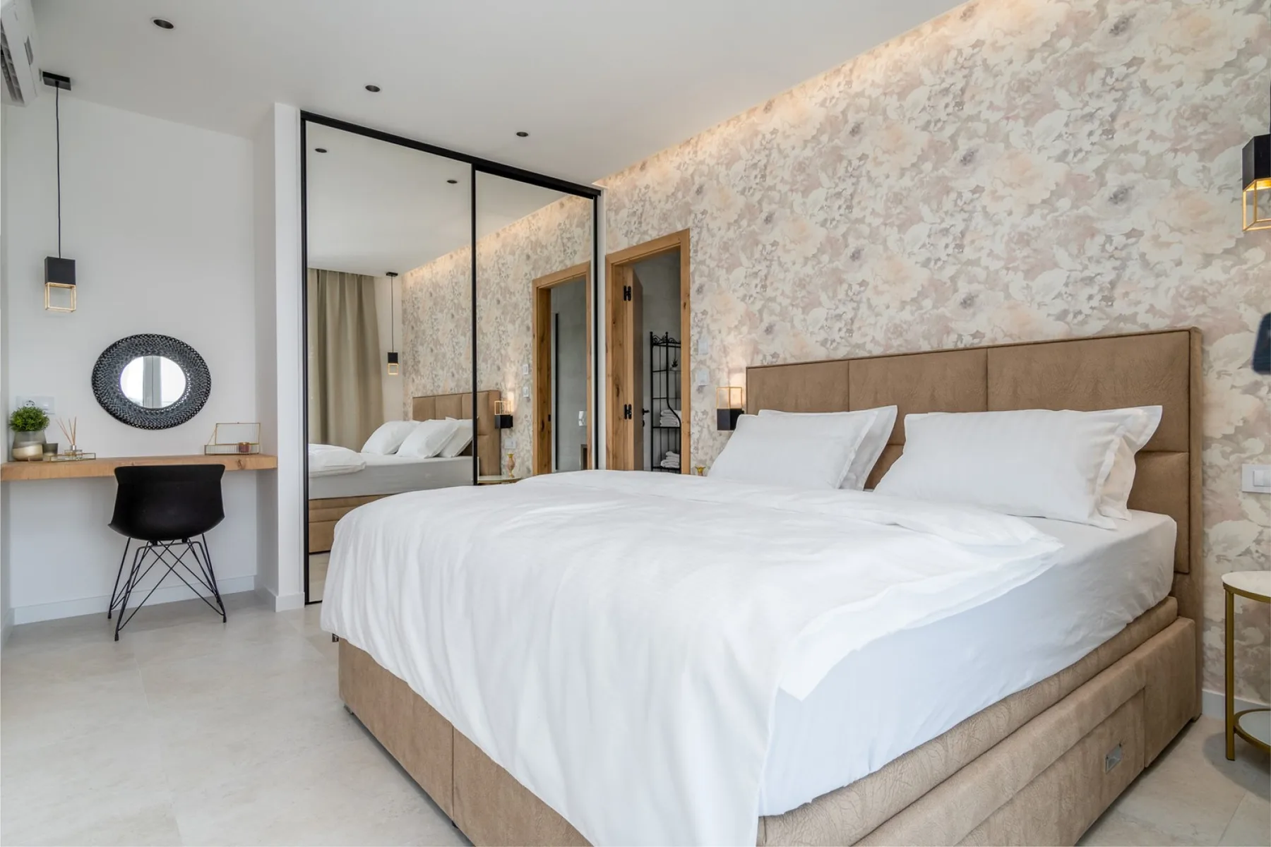 A bedroom with a large bed, white bedding, and a desk beside a round mirror.