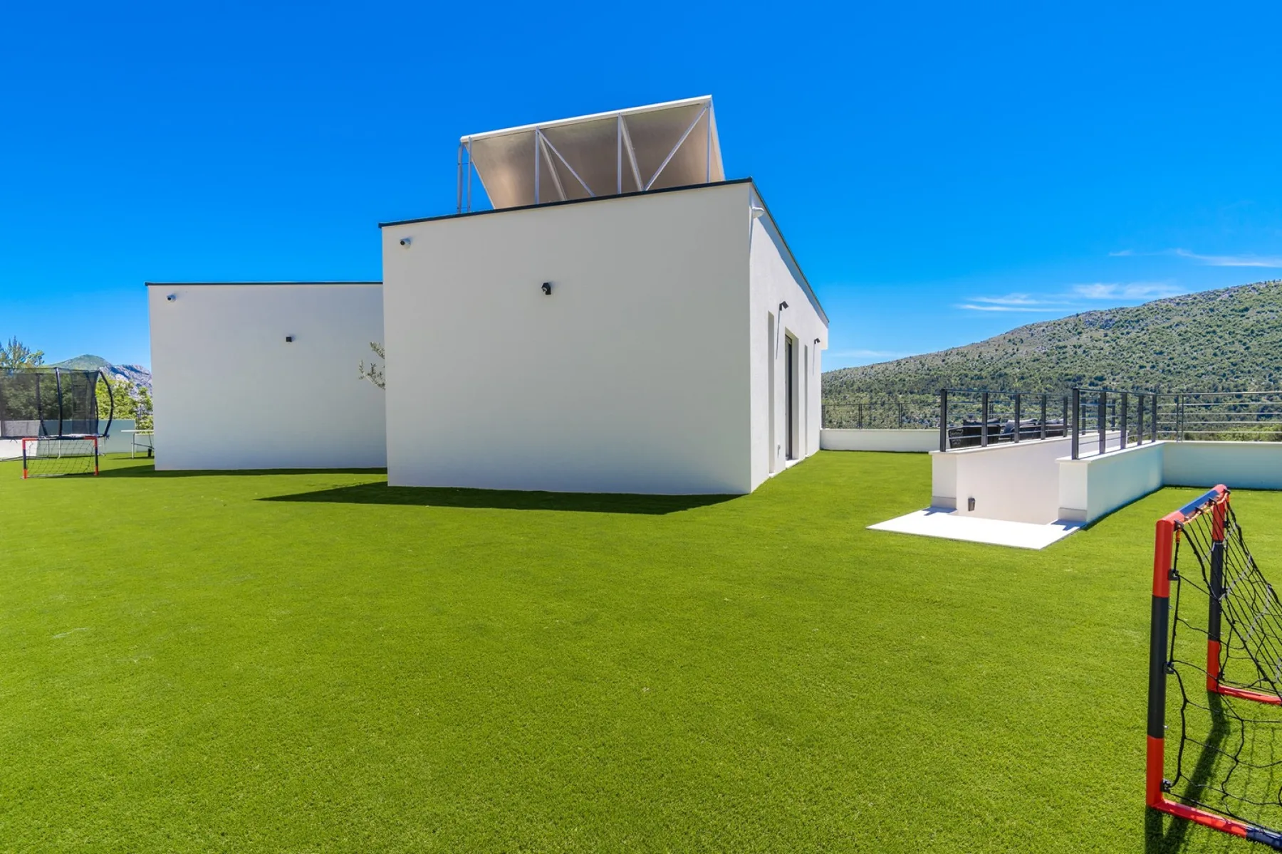 A white modern building stands beside a broad green lawn under a clear blue sky.