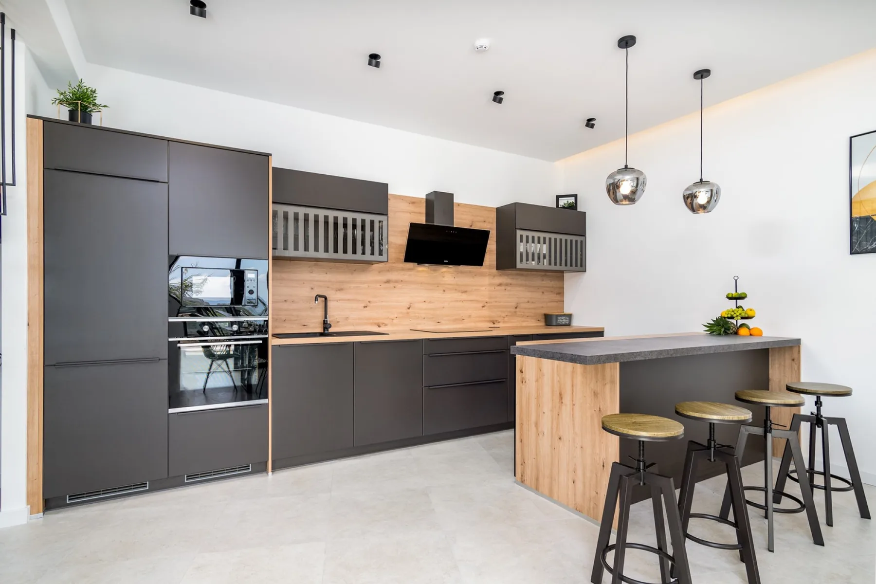 A modern kitchen with dark cabinets, a wood backsplash, and a breakfast bar.