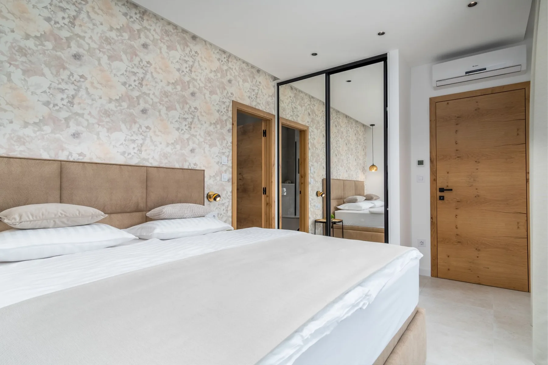 A bedroom with a large bed, floral-patterned wallpaper, and mirrored wardrobe doors.