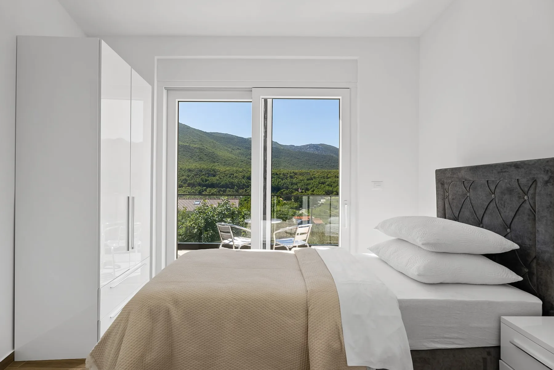 A bright bedroom with a neatly made bed and a window overlooking green hills.