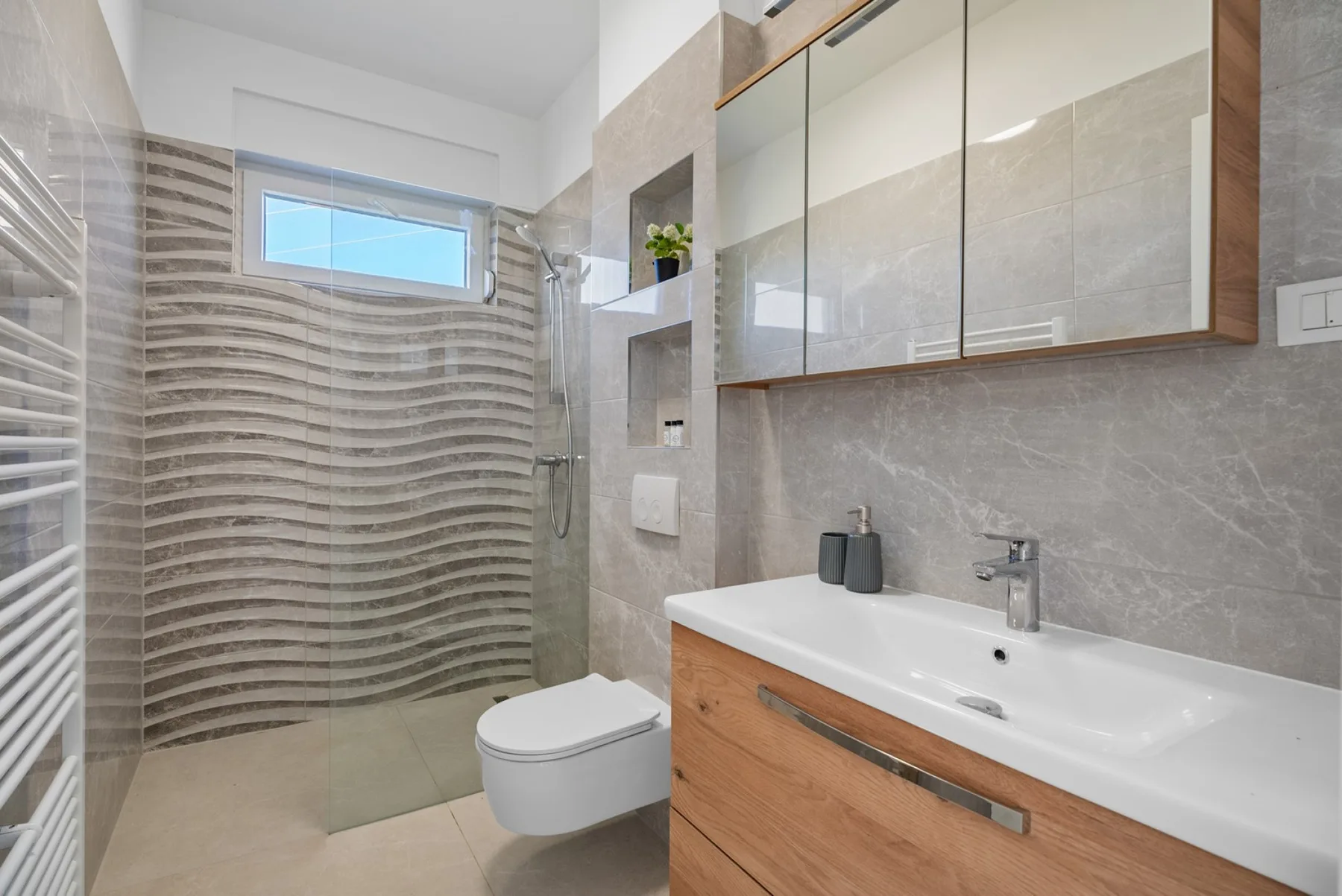 A modern bathroom with a glass shower, wall-mounted toilet, and vanity.