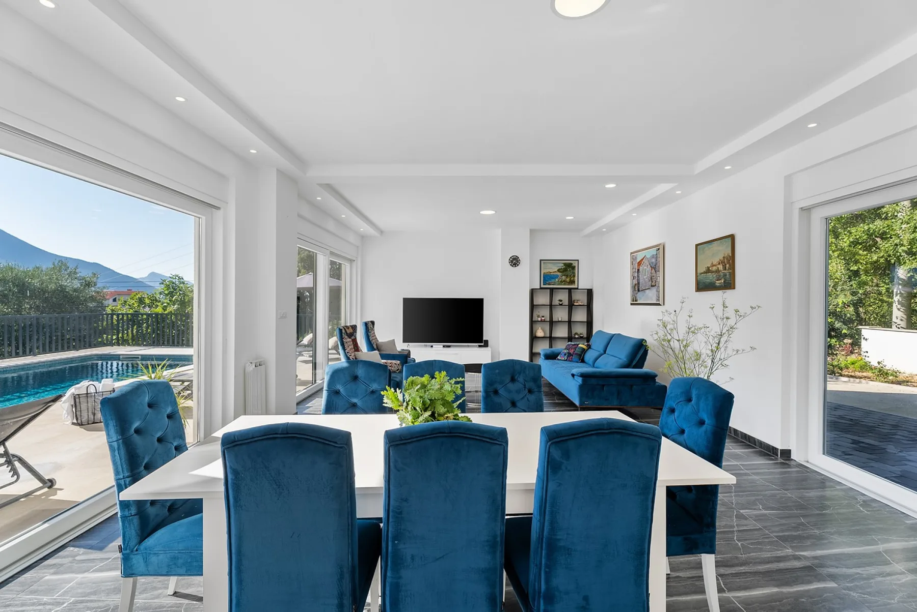A bright living and dining room opens onto a patio, with blue seating around a table.