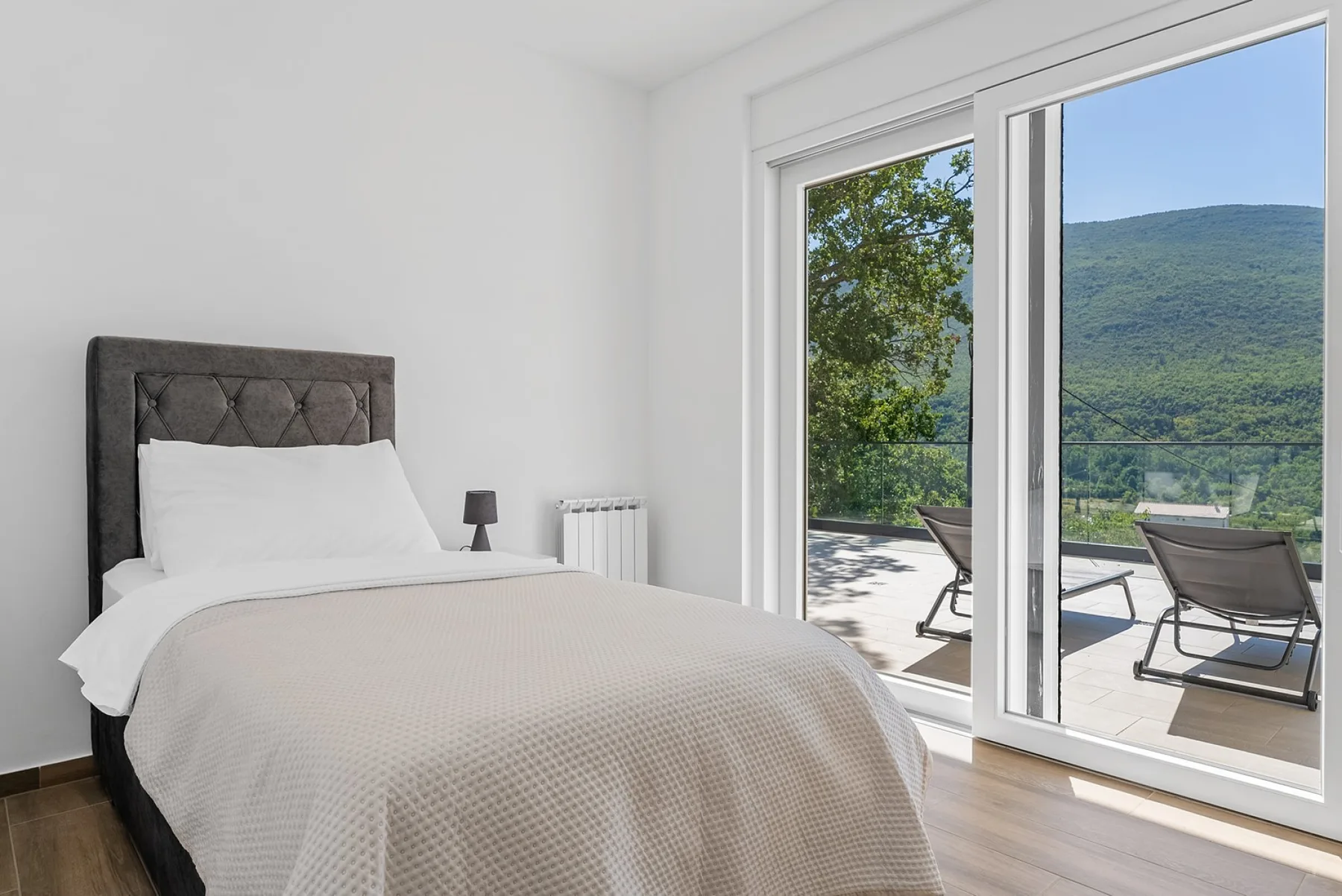 A bright bedroom with a bed beside large glass doors opening onto a terrace.