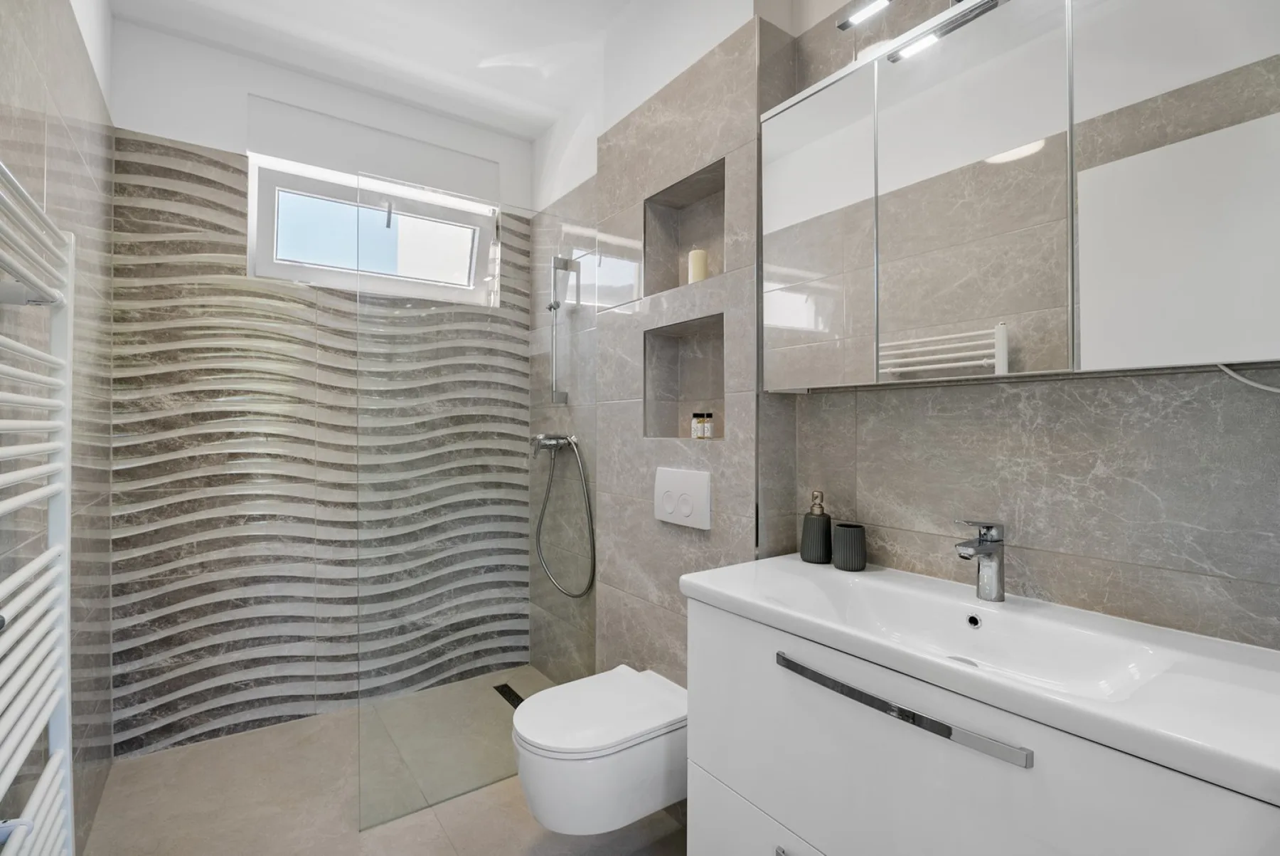 A modern bathroom with a glass shower, toilet, and sink beneath a large mirror.