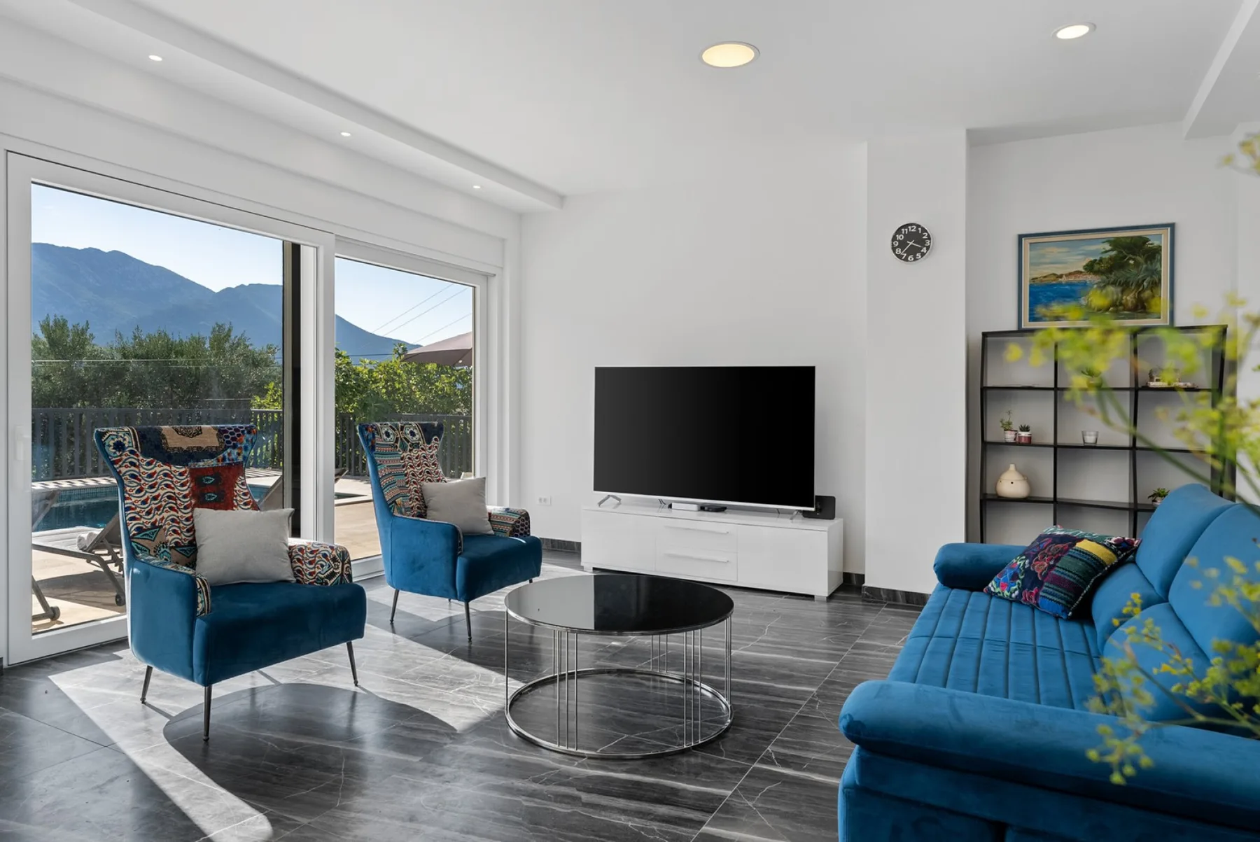 A bright living room with blue seating, a television, and large glass doors.