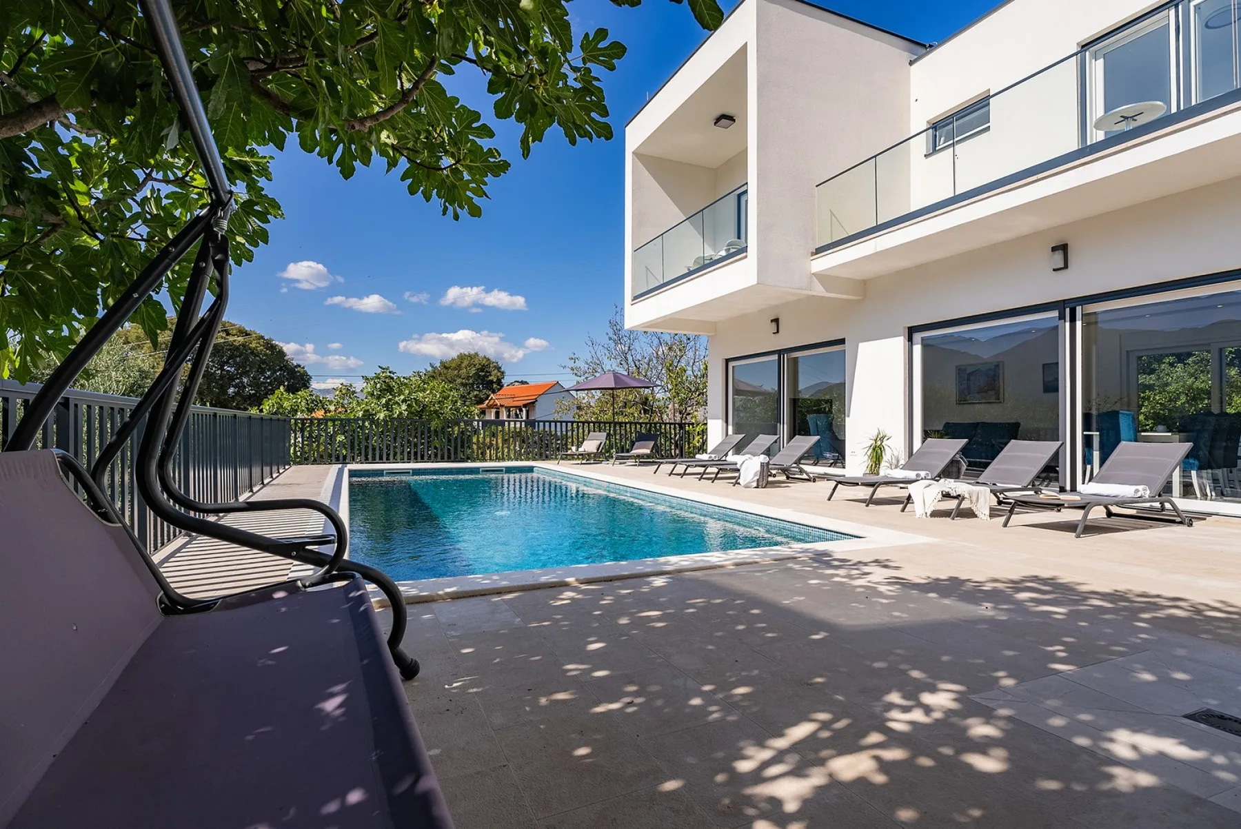 An outdoor swimming pool beside a modern white building, with lounge seating along the deck.