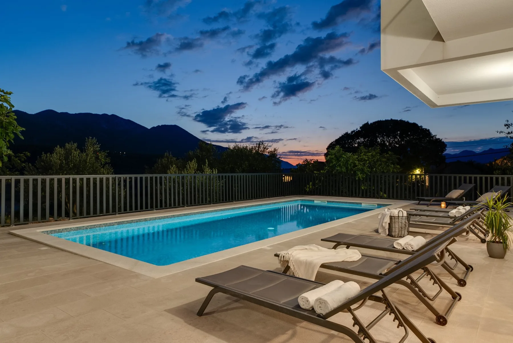 An outdoor swimming pool with lounge seating overlooks mountains at dusk.