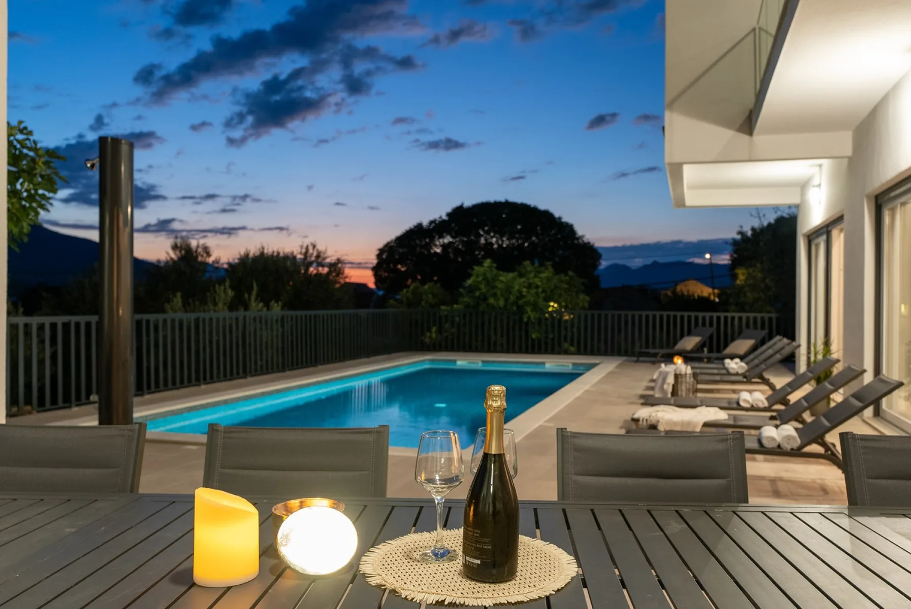 A poolside patio at dusk with outdoor seating and a lit table.