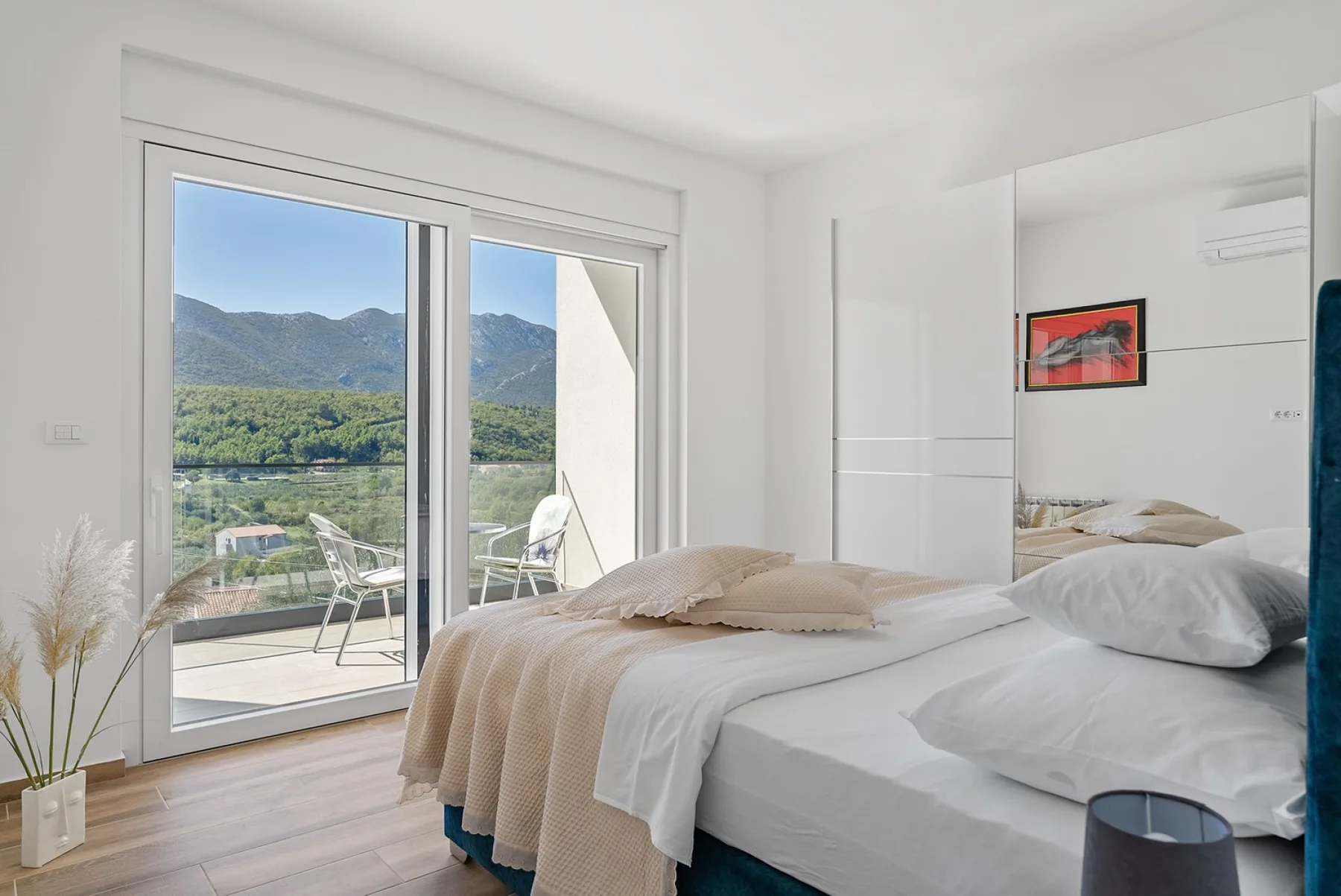 A bright bedroom with a bed beside large windows overlooking green hills.